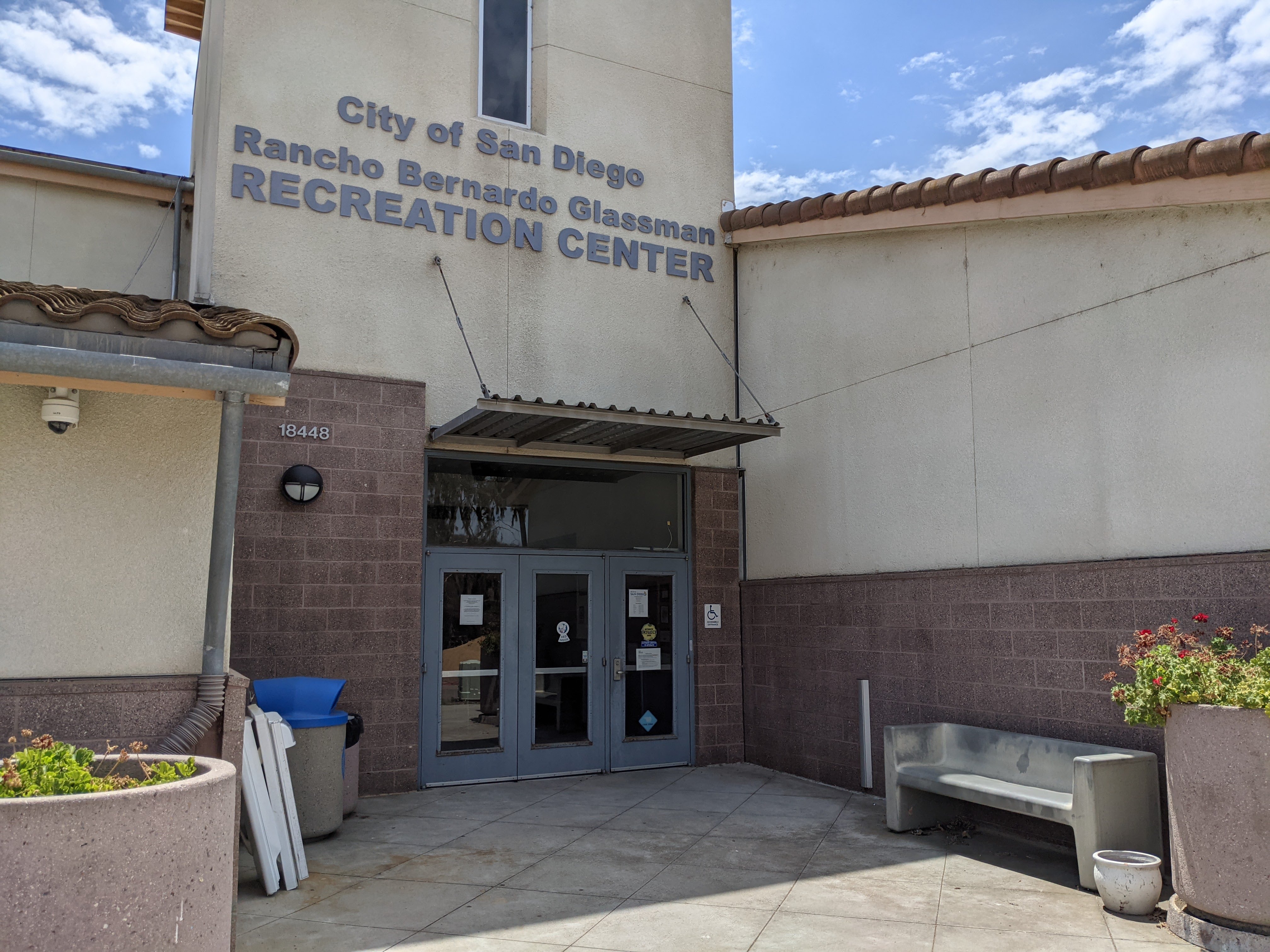 Glass entrance doors of a brick and stucco recreation center building with a metal canopy.