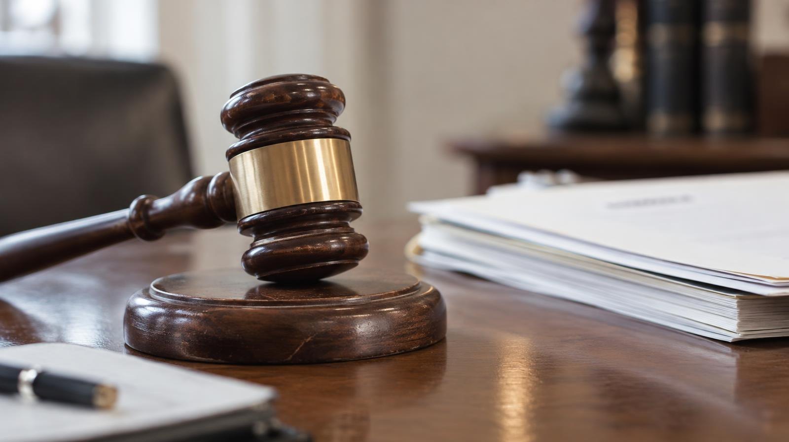A wooden gavel resting on its sound block beside stacked documents on a table.