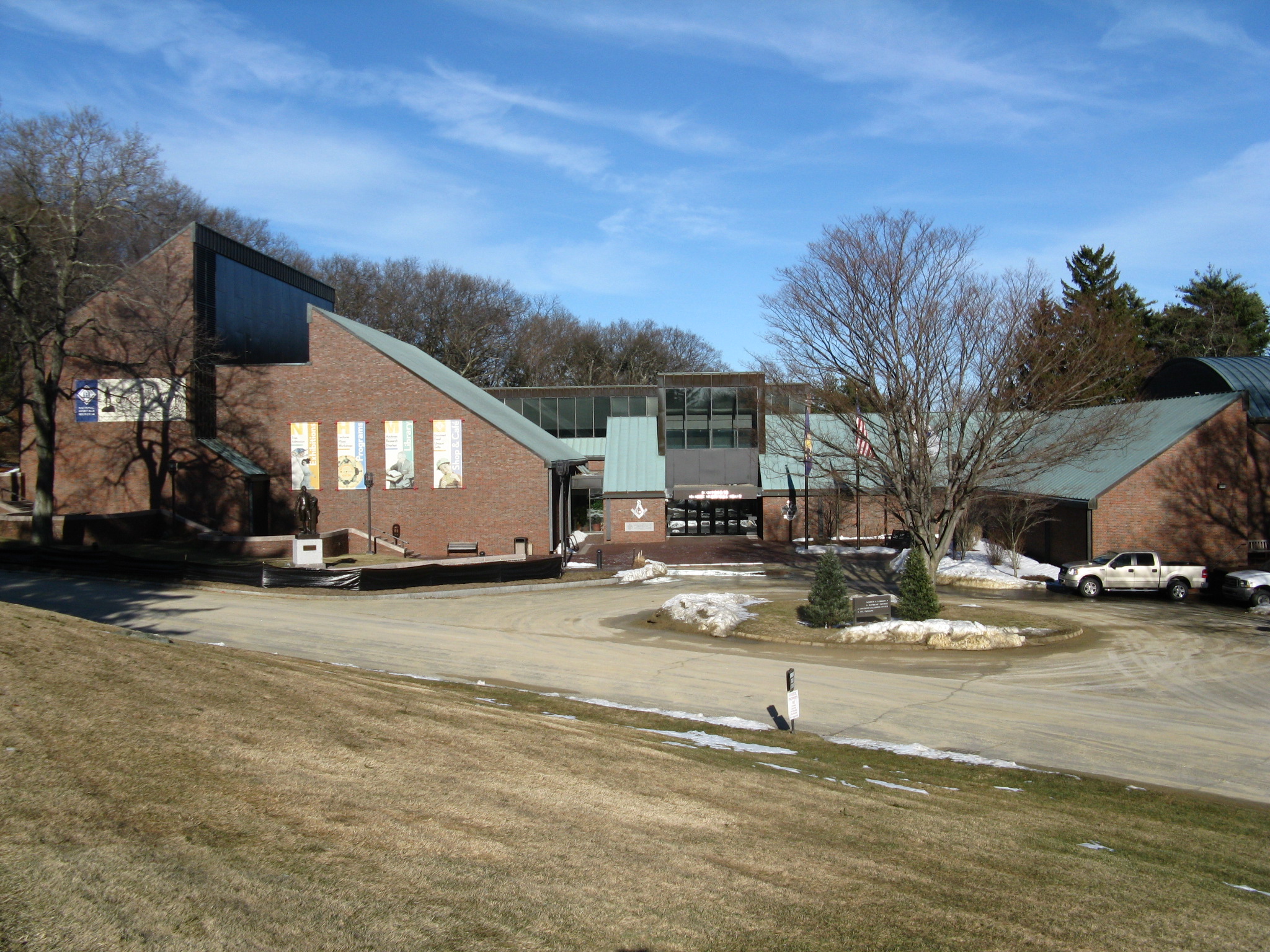 Brick and glass building with a green angular roof, bare trees, and snow on the ground.