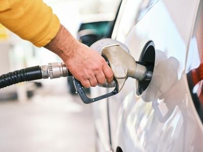 A hand in a yellow sleeve holds a fuel nozzle inserted into a white car's gas tank.