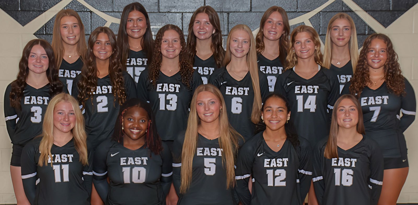 About 18 young women in dark green 'EAST' volleyball uniforms posed in three rows for a team photo.