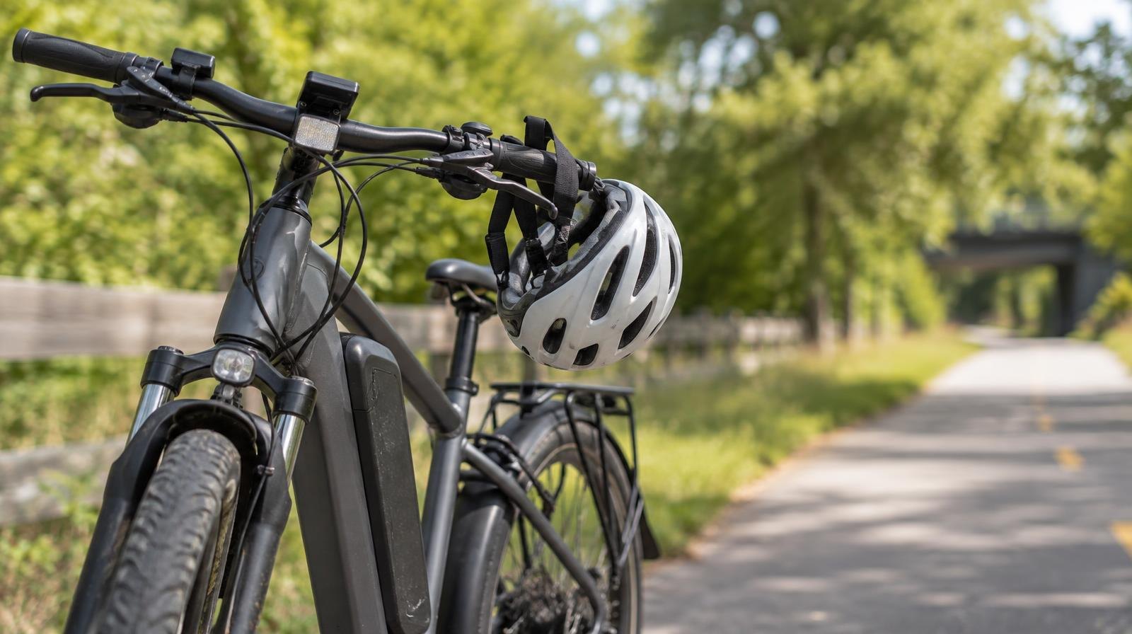 Electric bicycle parked beside a paved path with a helmet on the handlebars.