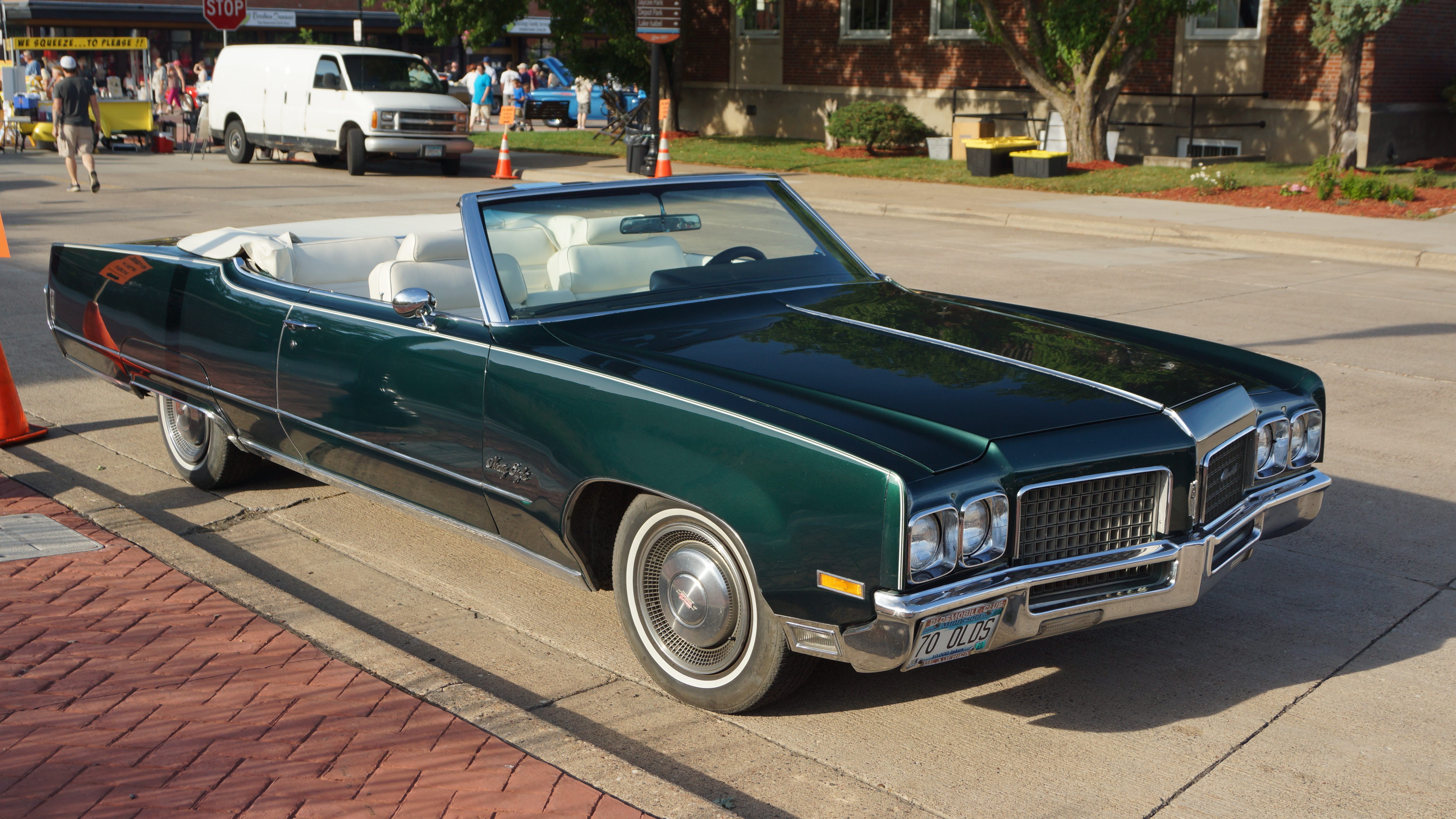 Dark green classic convertible with white interior parked at an outdoor car show.