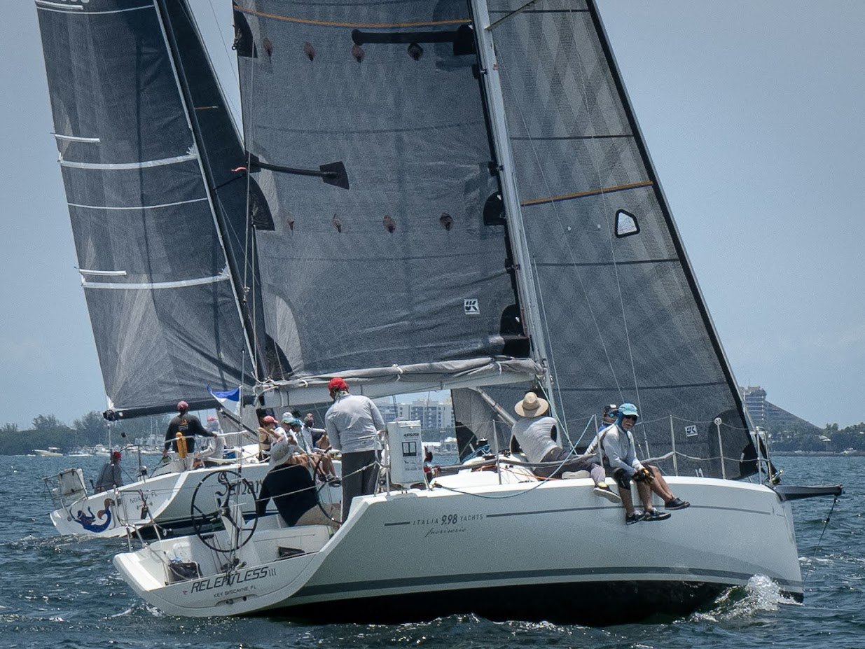 Two racing sailboats with large grey sails sailing close together on open water.