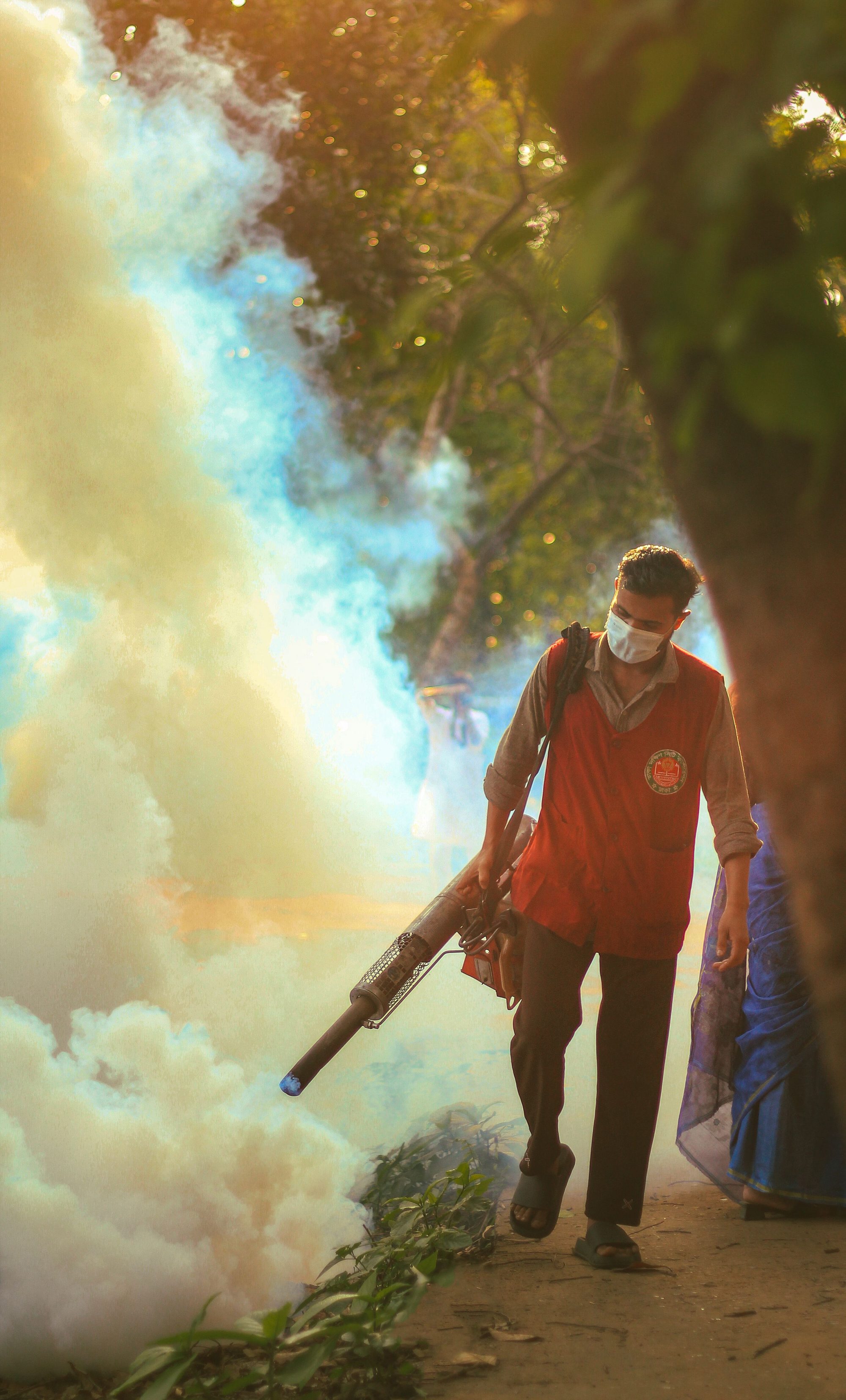 A worker performs fogging to control mosquitoes in a city park during the afternoon.