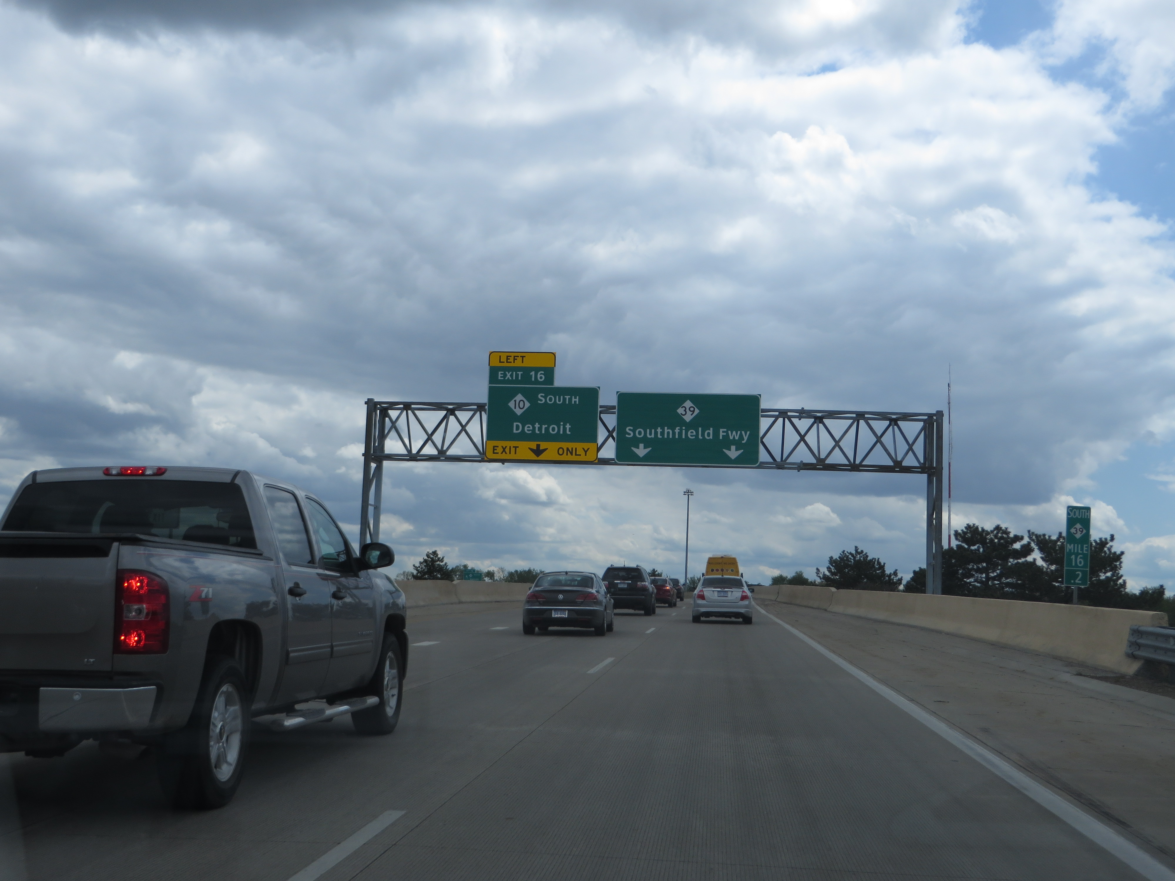 Overhead green highway signs on a multi-lane freeway with vehicles in traffic.