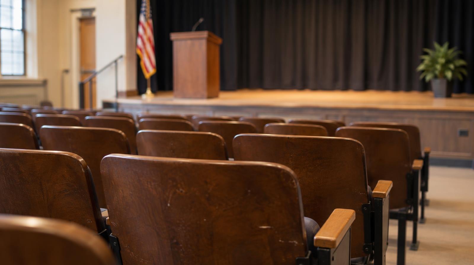 Empty rows of upholstered auditorium seats face a bare stage.