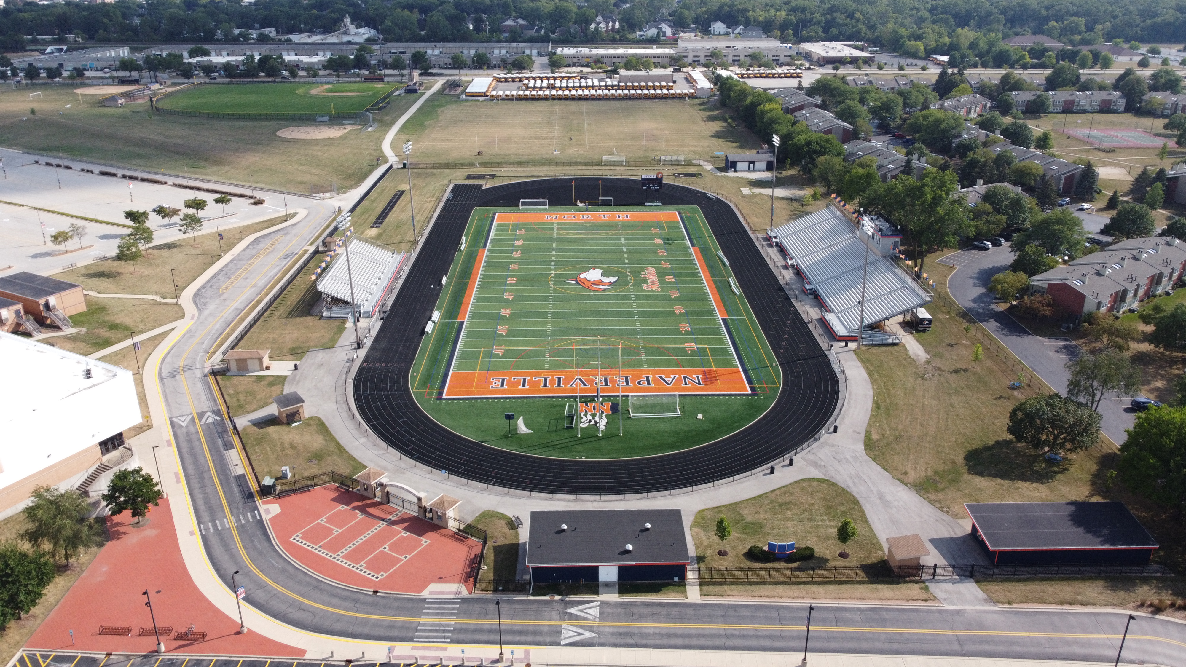 Aerial view of a high school football field with orange turf and a black running track.