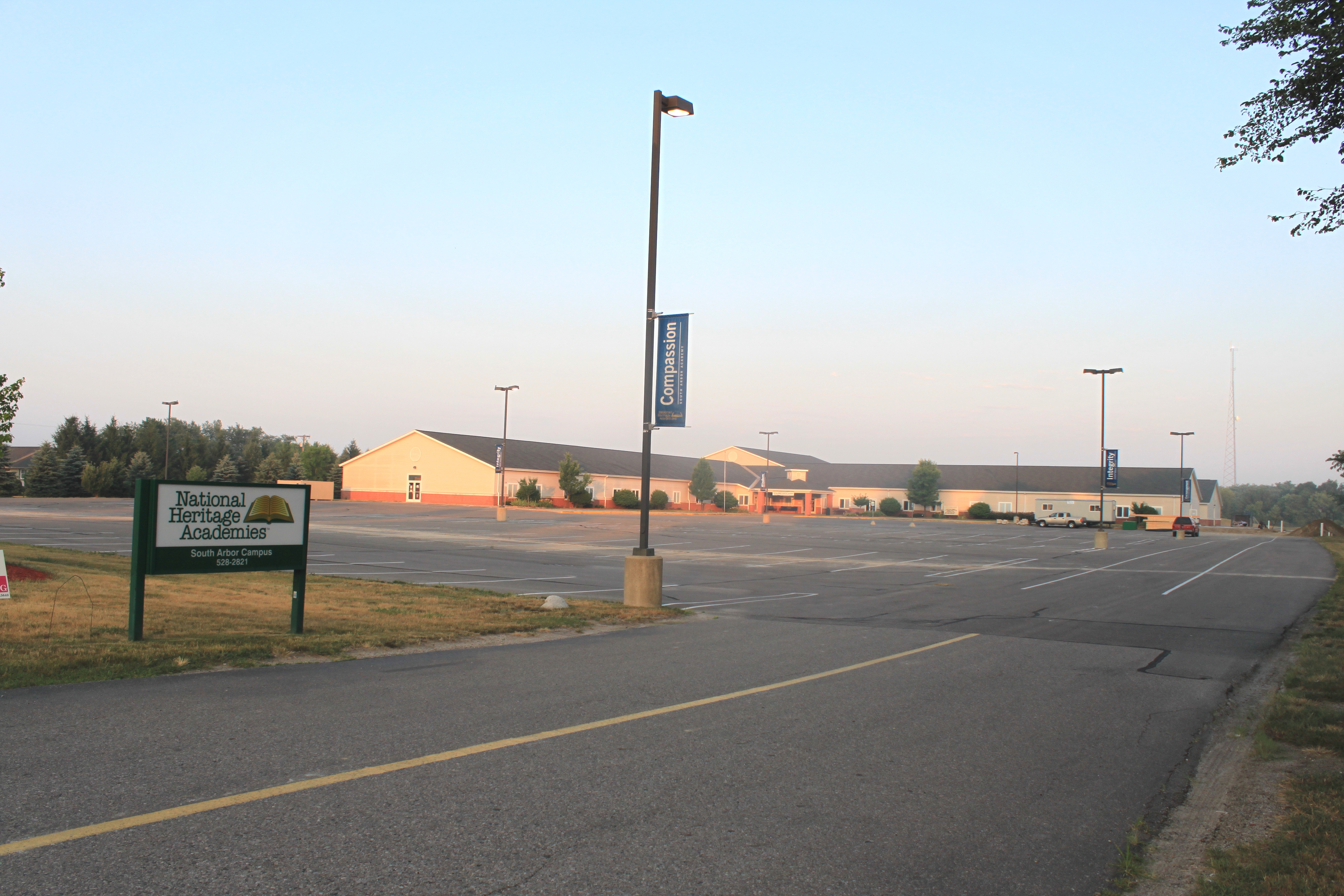 Single-story school building with a large parking lot and a sign in front.