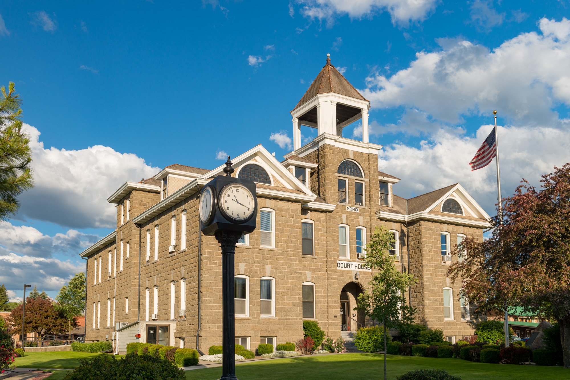 Historic stone courthouse with a clock tower and American flag under a blue sky