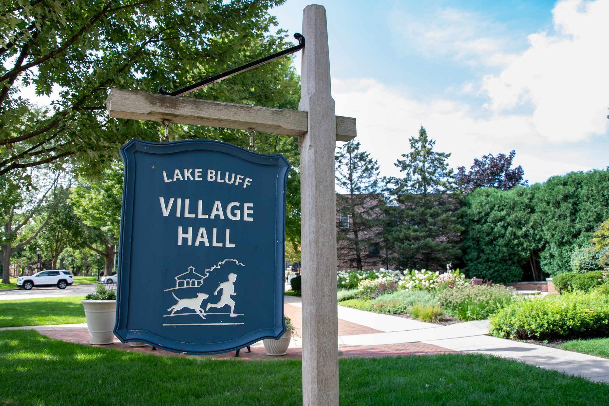 Navy blue village hall sign hanging from a wooden post outdoors