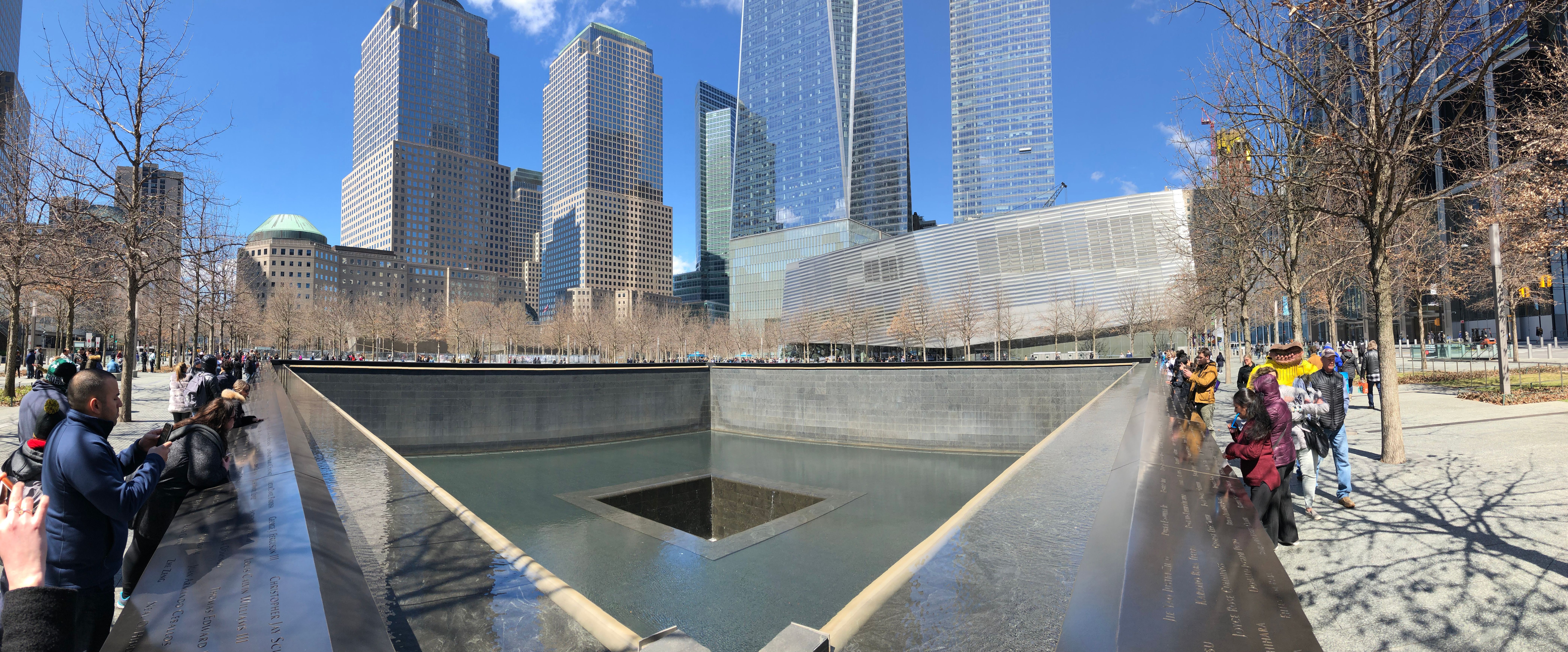 Two large reflecting pools at the 9/11 Memorial, surrounded by visitors and bare trees.