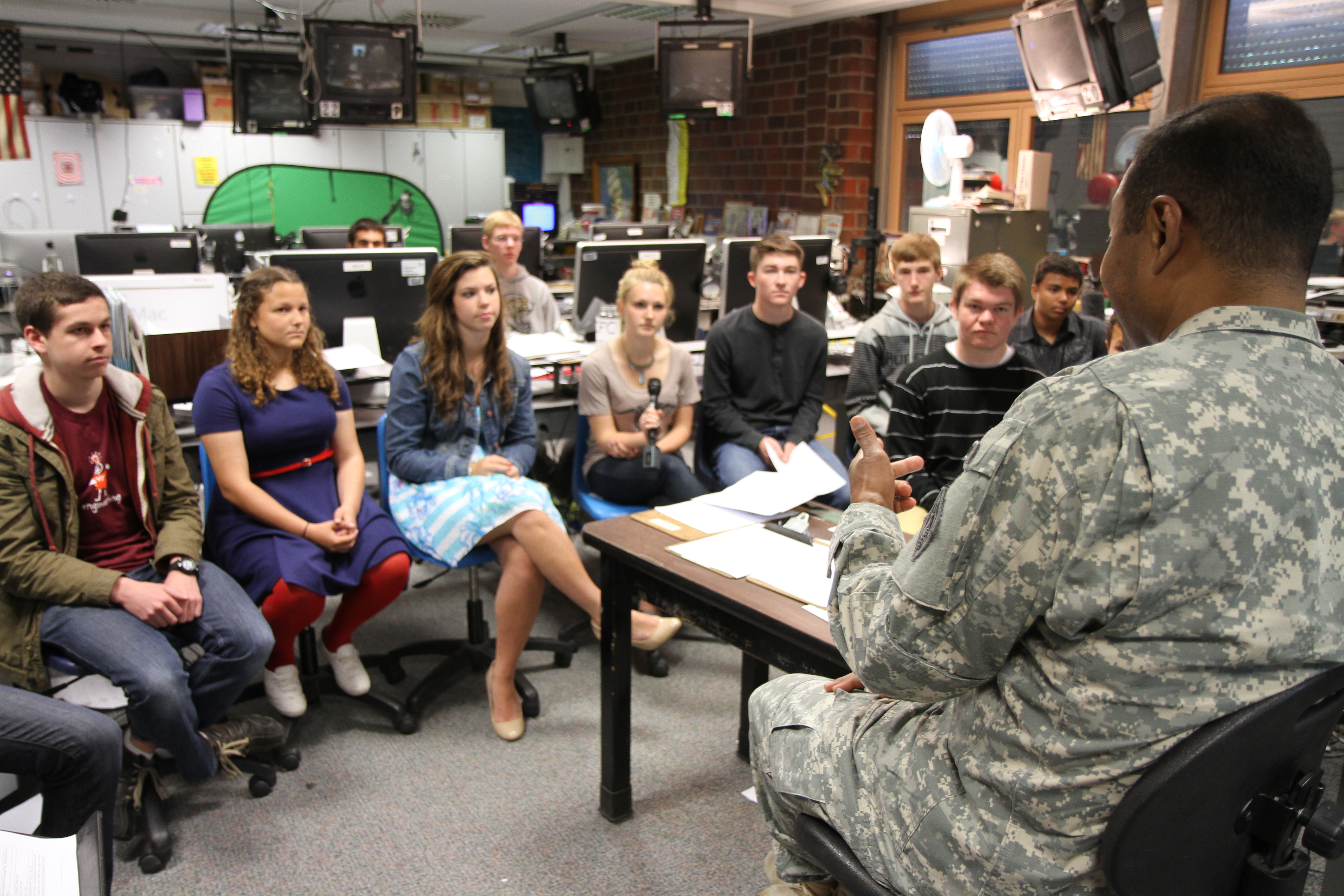 Students in a school media production classroom with cameras, computers, and a green screen.