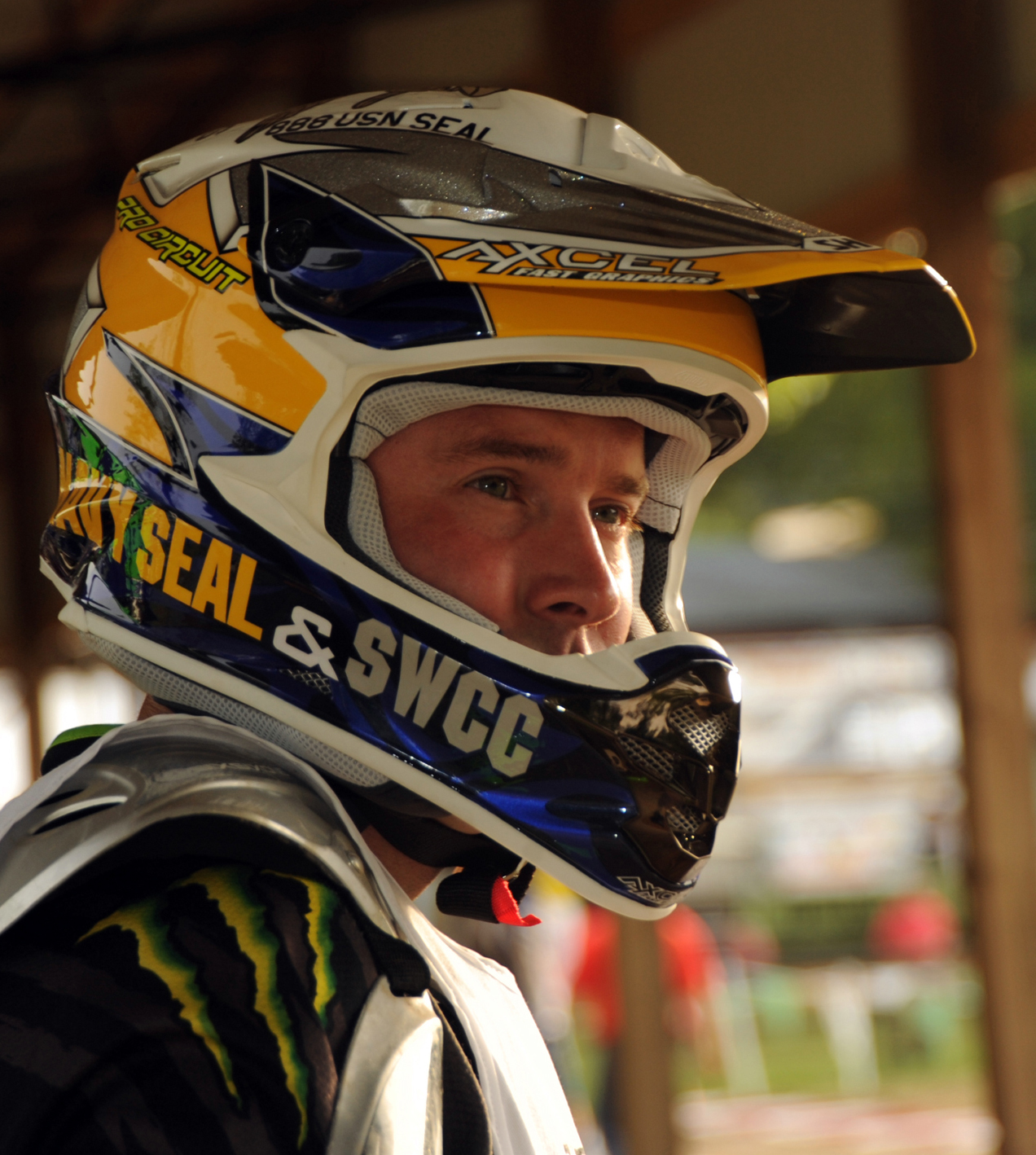 A motocross rider wearing a full-face helmet and racing jersey at a race venue.