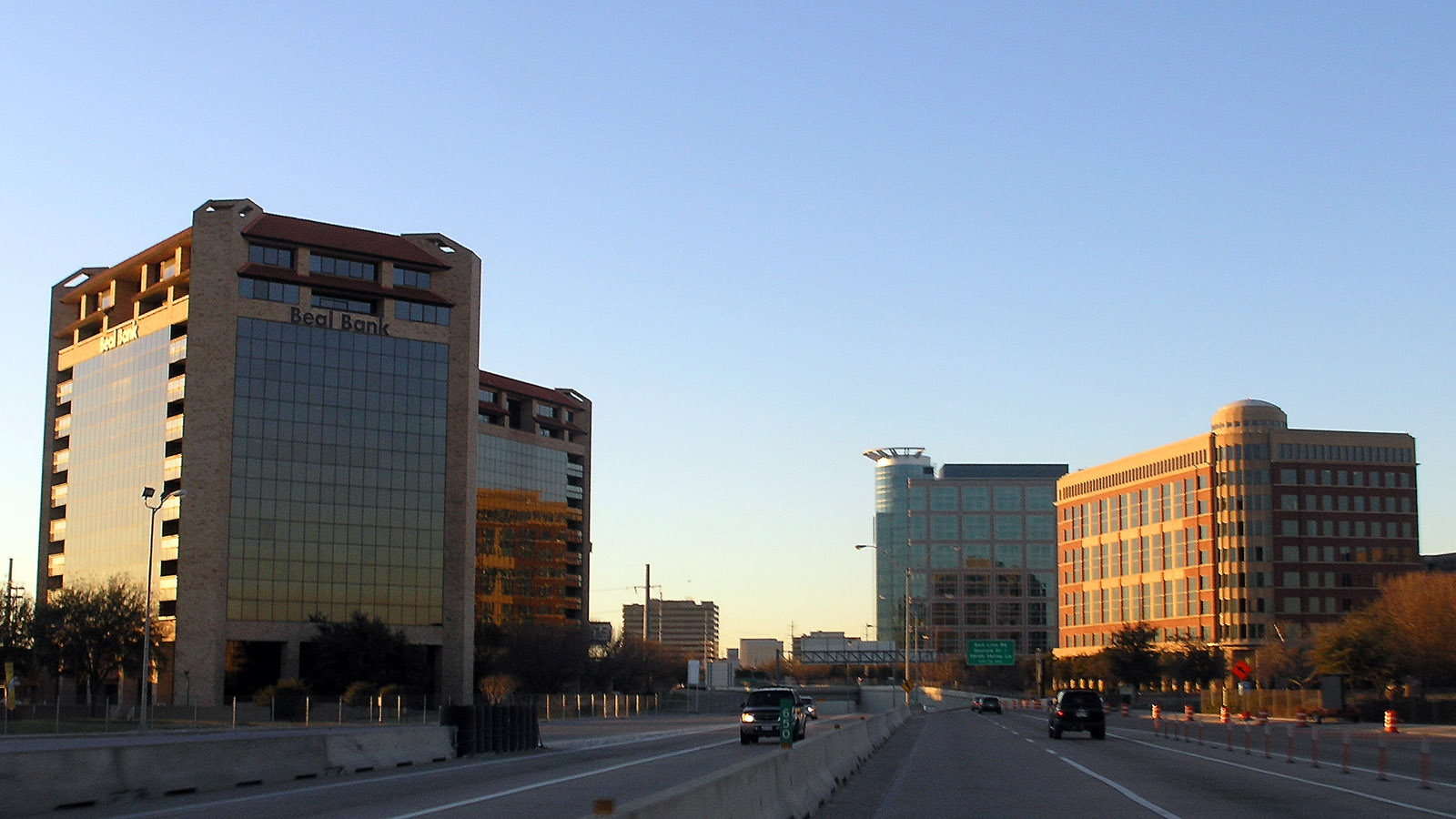 Multi-lane divided tollway flanked by mid-rise office buildings in the Dallas-Fort Worth area.