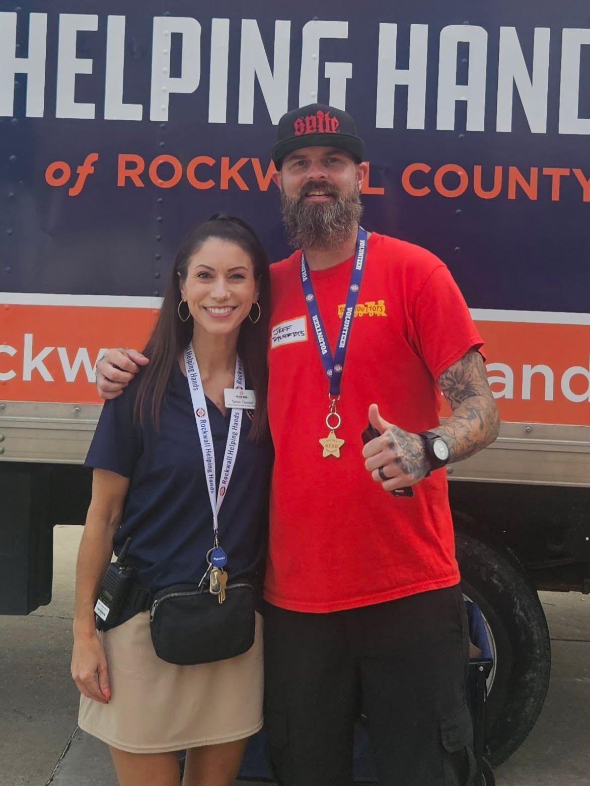 Two people pose in front of a Helping Hands of Rockwall County vehicle.
