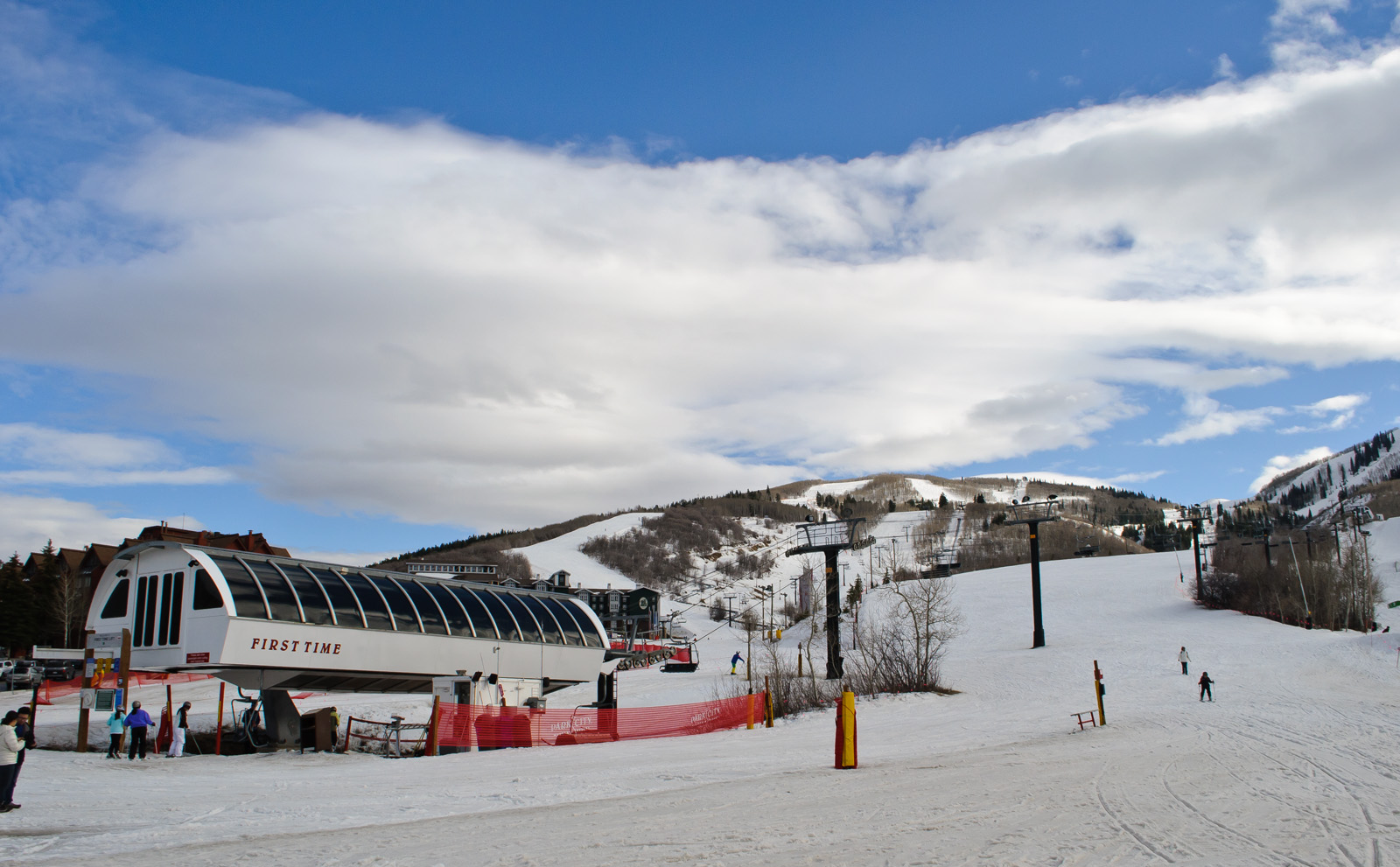 Snow-covered ski slope with a chairlift terminal building and skiers on a partly cloudy day.