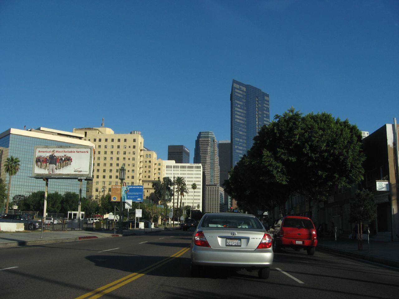 Cars traveling along a wide palm-tree-lined boulevard with commercial buildings and distant skyscrapers.