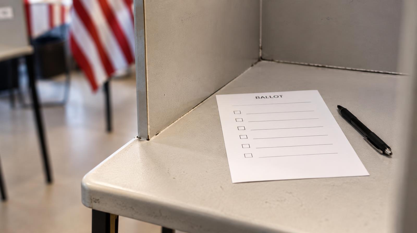 A blank paper ballot inside a voting booth with a black pen resting beside it.