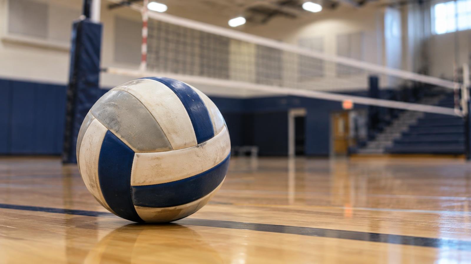 A volleyball resting on a hardwood gymnasium floor near the net.