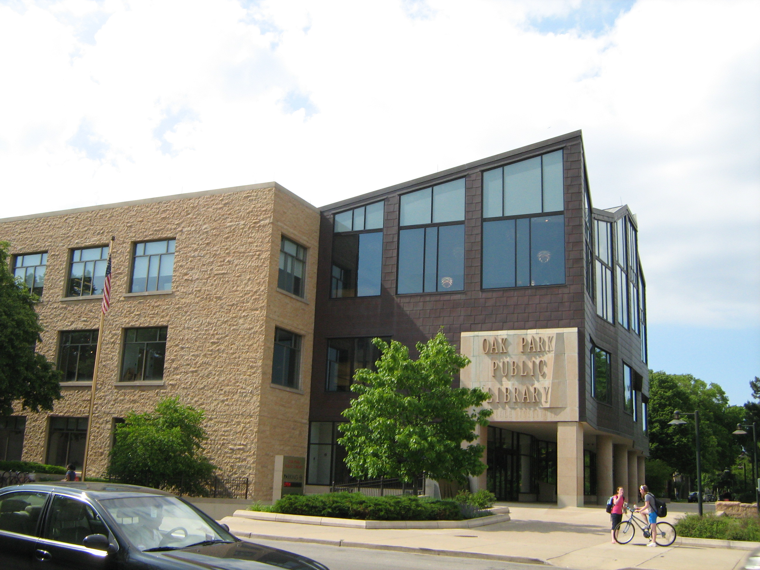 Two-story library building with stone facade, signage, and an American flag.