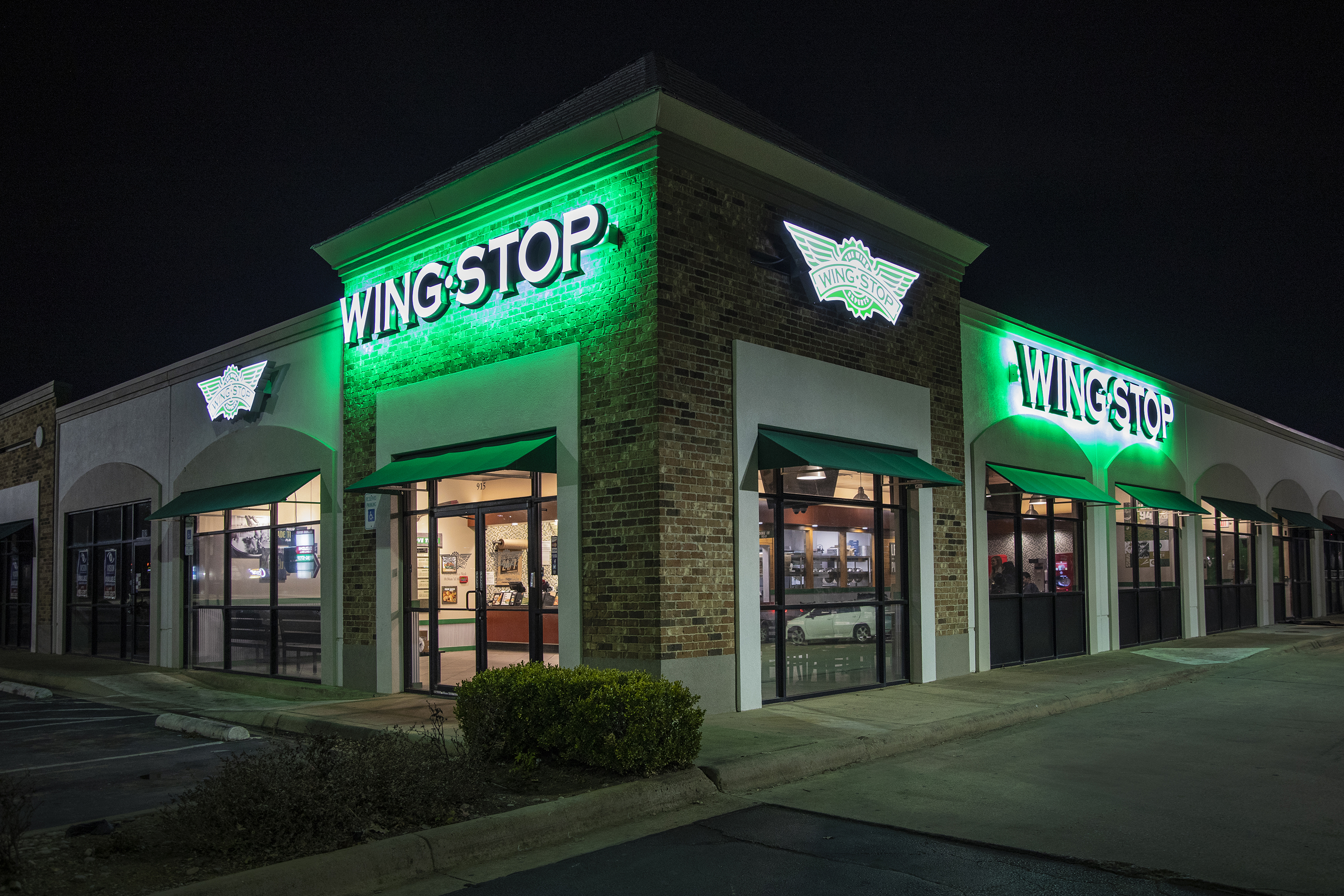 Wingstop restaurant exterior at night with green neon sign and brick facade.