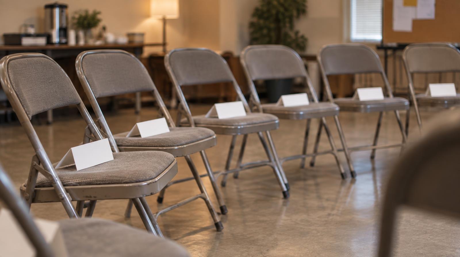 Empty folding chairs arranged in a semicircle in a community meeting room.
