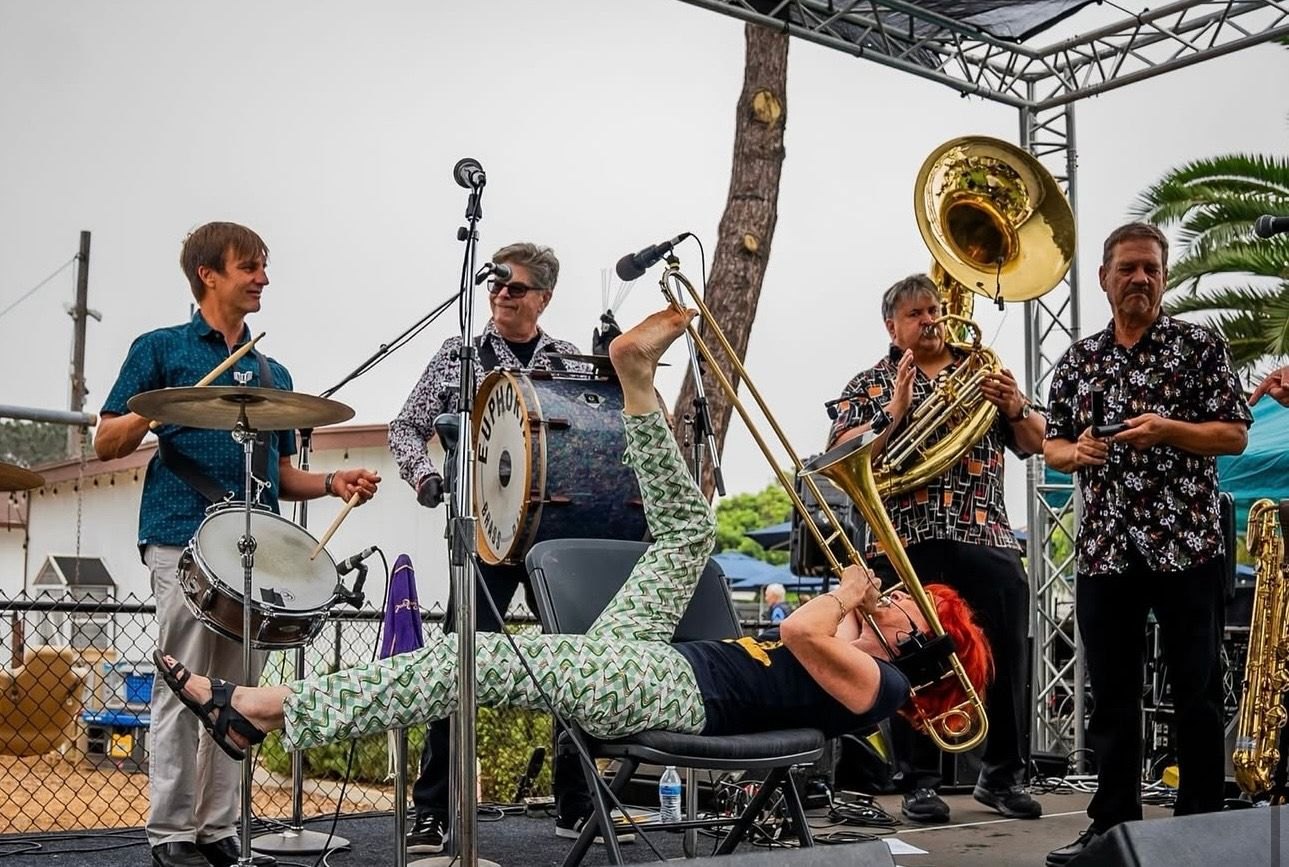 Brass band musicians perform on an outdoor stage under an overcast sky.