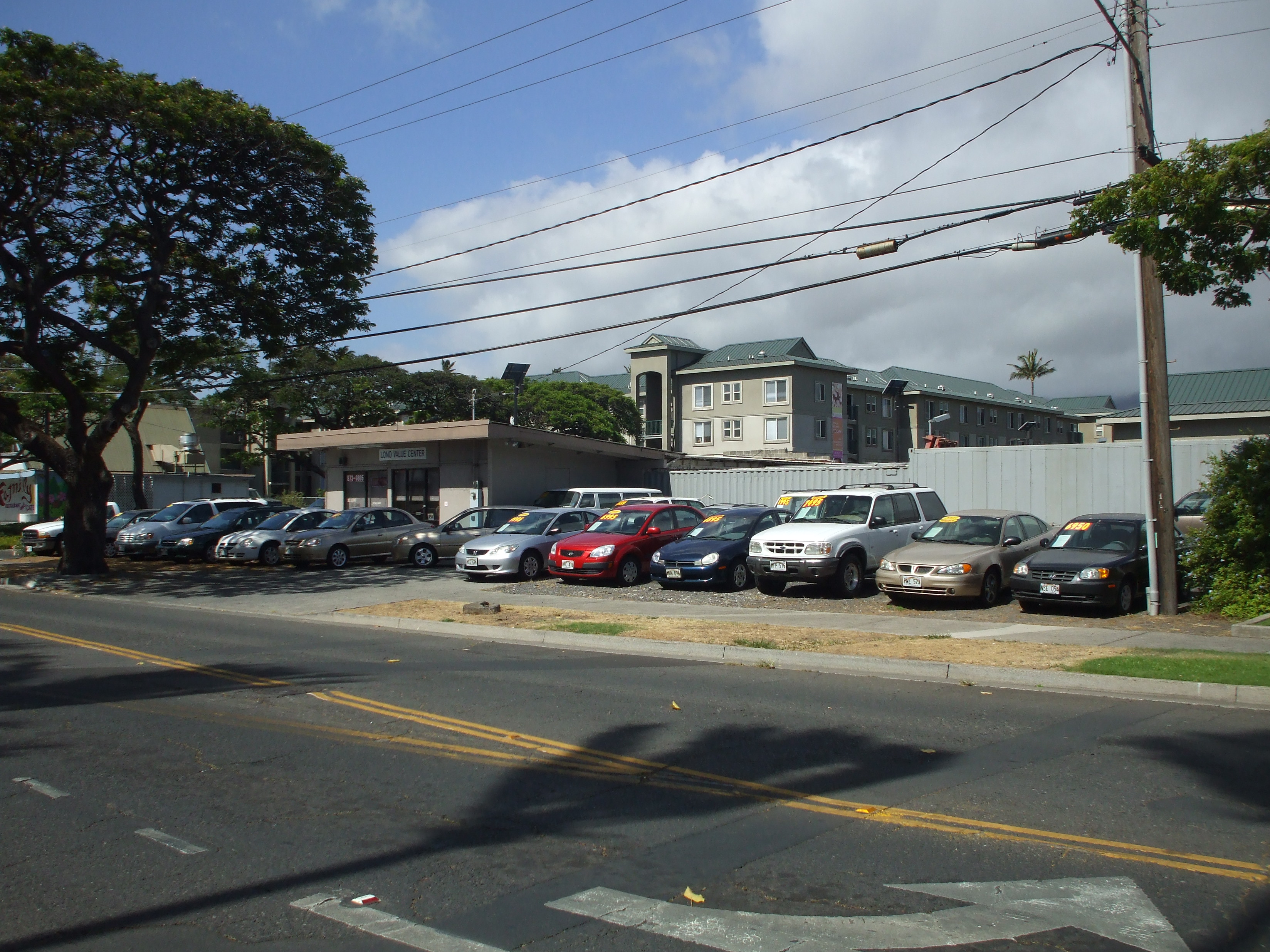 Rows of used cars parked on a gravel lot beside a small building.