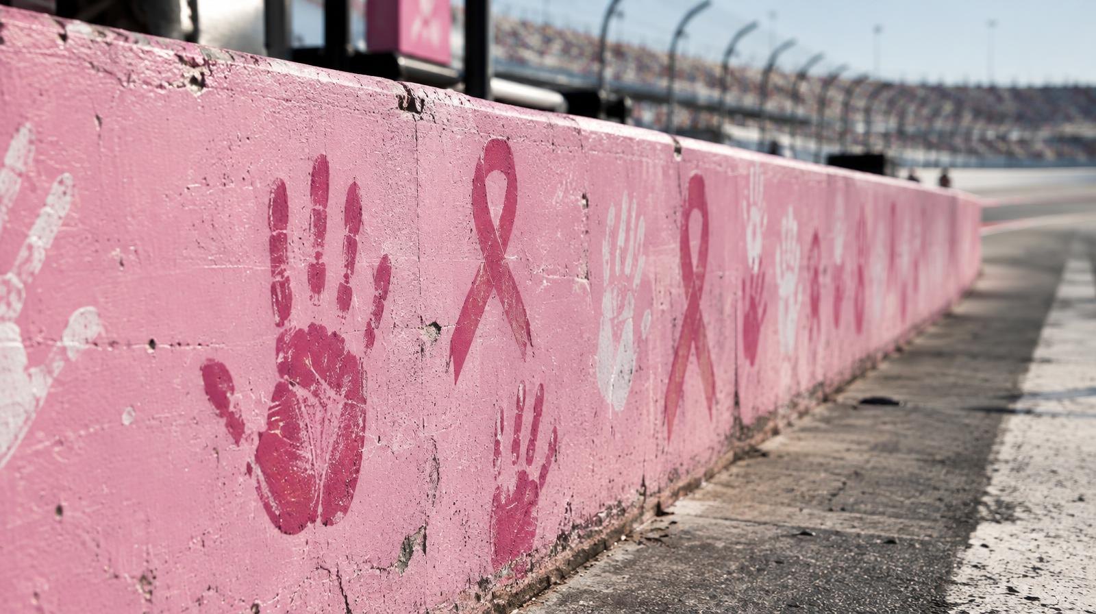 Pink-painted concrete pit wall with ribbon and handprint decorations at a racetrack.