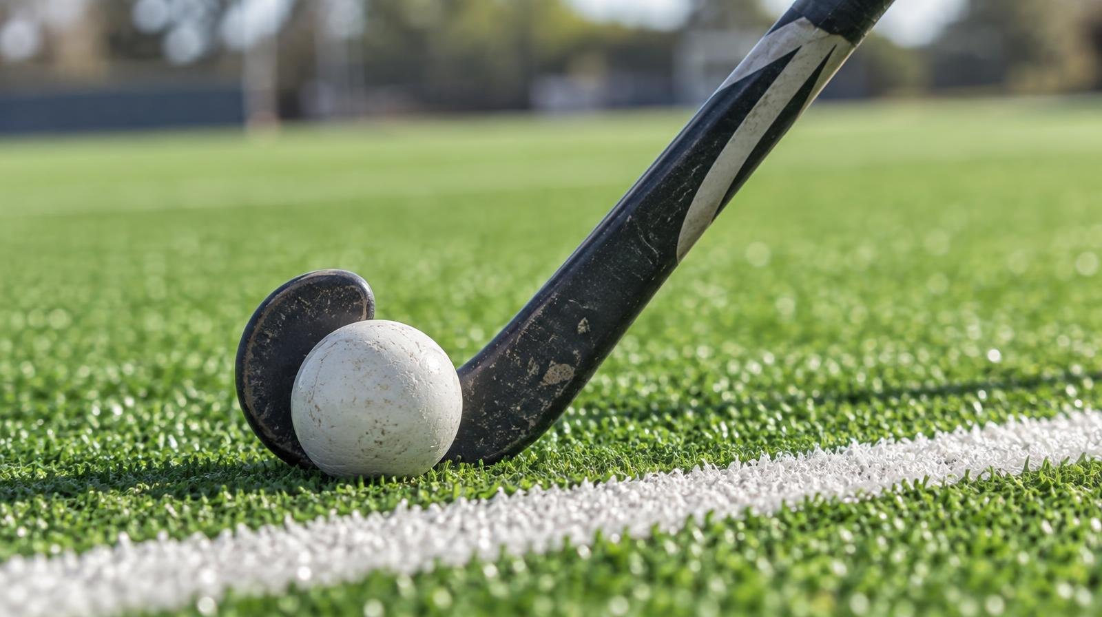 A field hockey stick and ball resting on green artificial turf beside a white line.