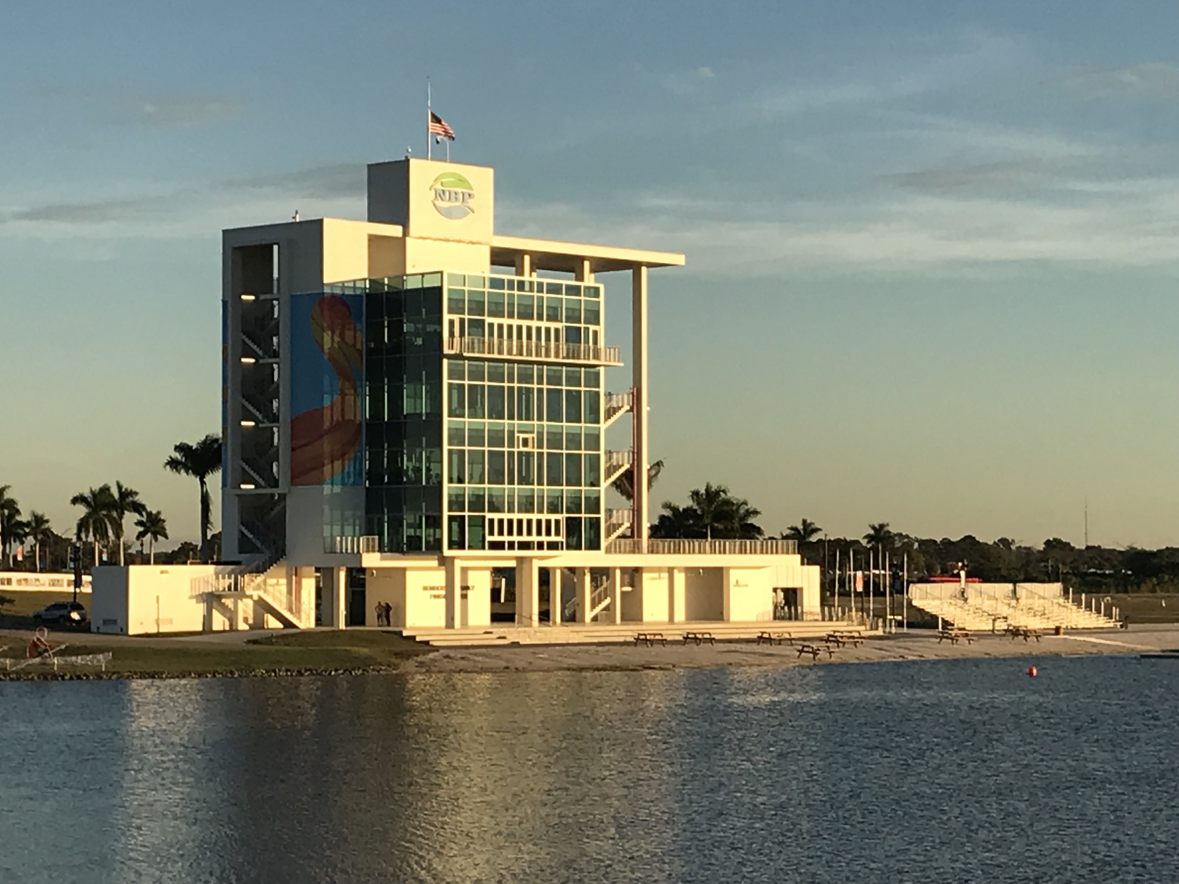 Modern glass and white tower building at the edge of a calm lake at golden hour.