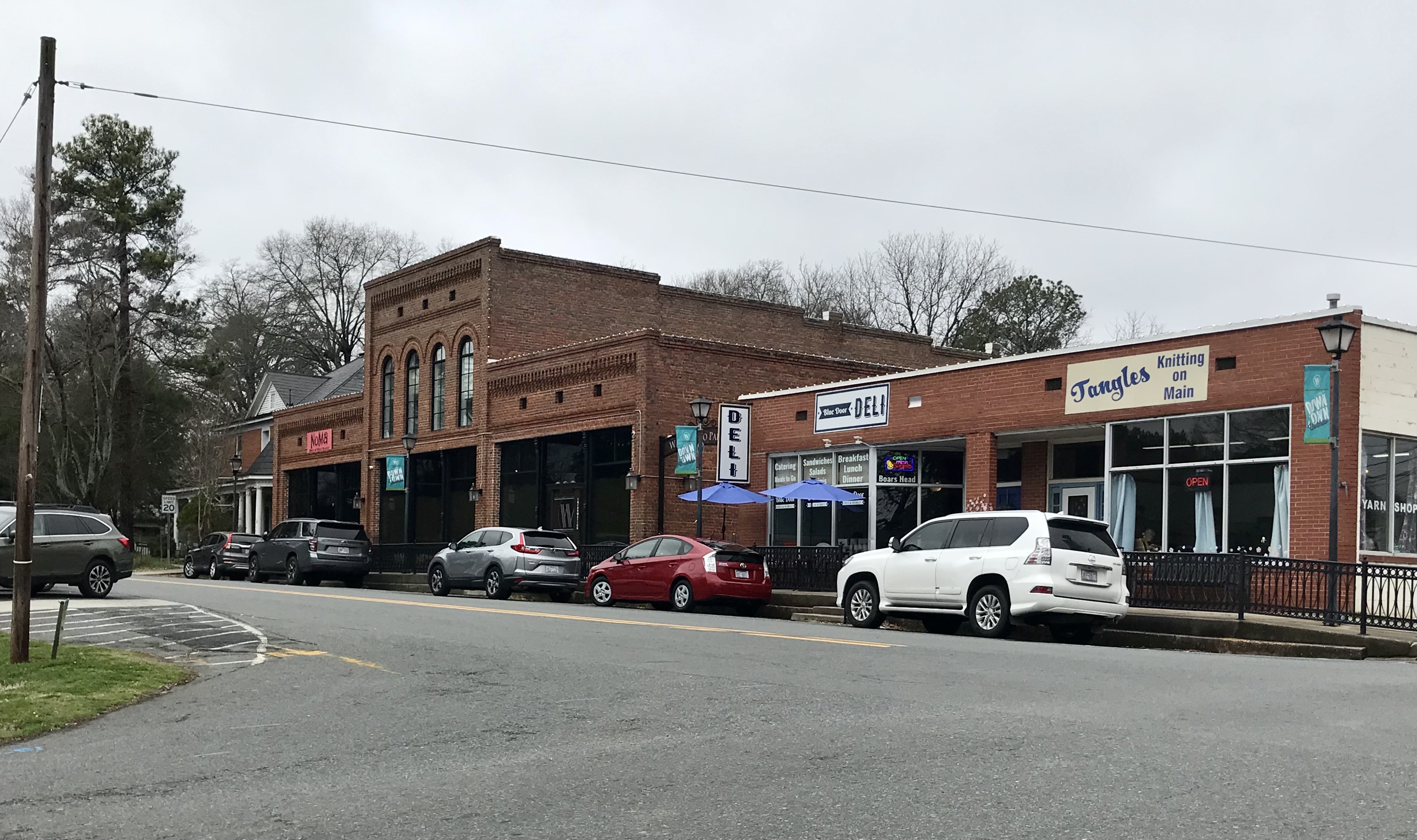 Brick storefronts and parked cars along a small-town street with bare trees.