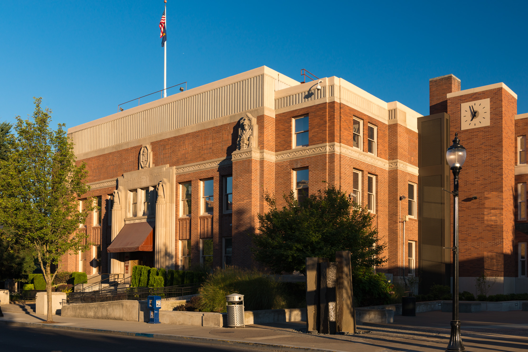Red brick courthouse with Art Deco clock tower and American flag against a blue sky.