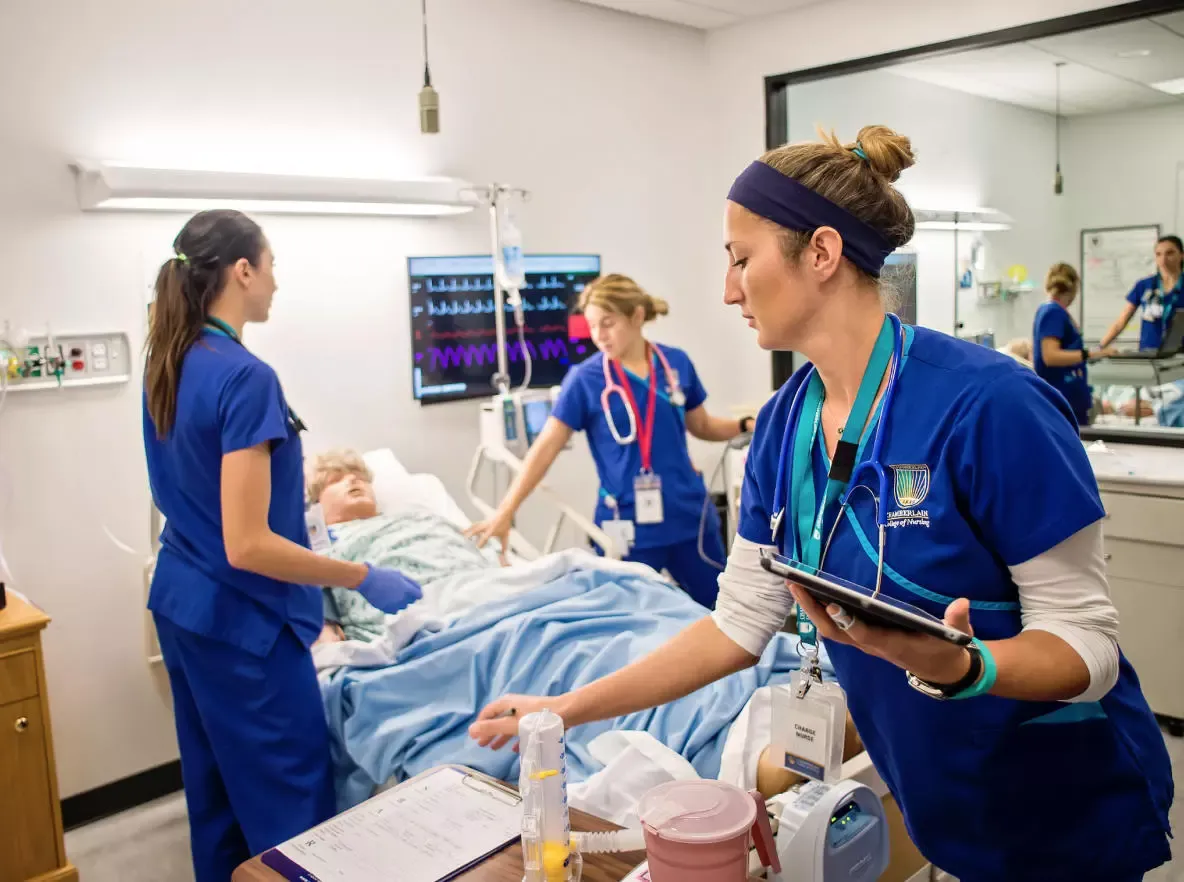three nurses in training around a hospital bed