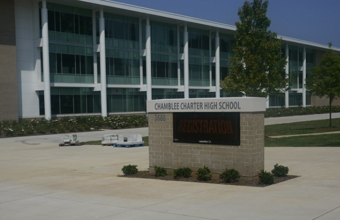 Modern multi-story school building with glass windows, a flagpole, and a manicured lawn.