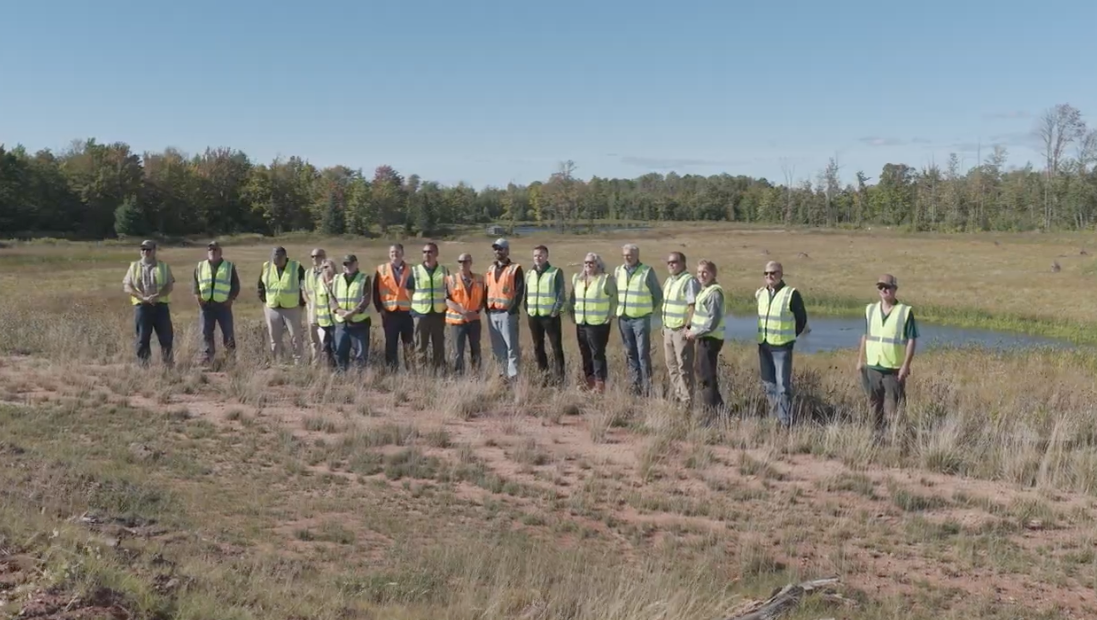 Local officials wearing safety vests gather at the site of a potential mine.