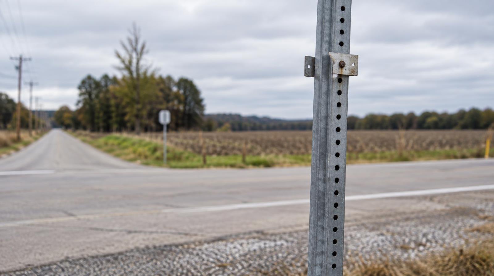 Bare metal sign post with empty mounting hardware at a rural roadside intersection.