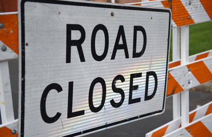 Road Closed sign mounted on orange and white striped construction barricades.