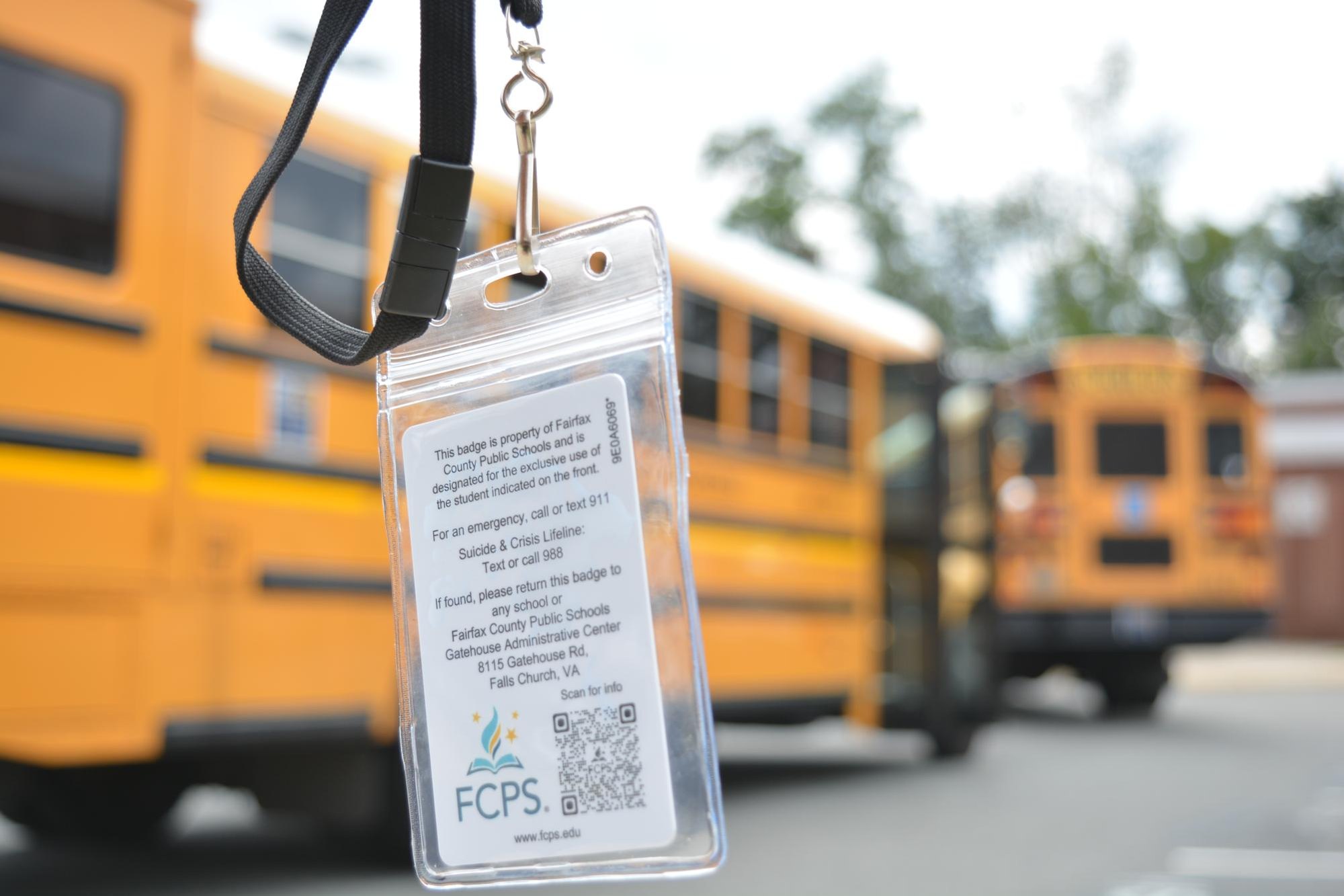 An FCPS student ID badge on a black lanyard with yellow school buses in the background.