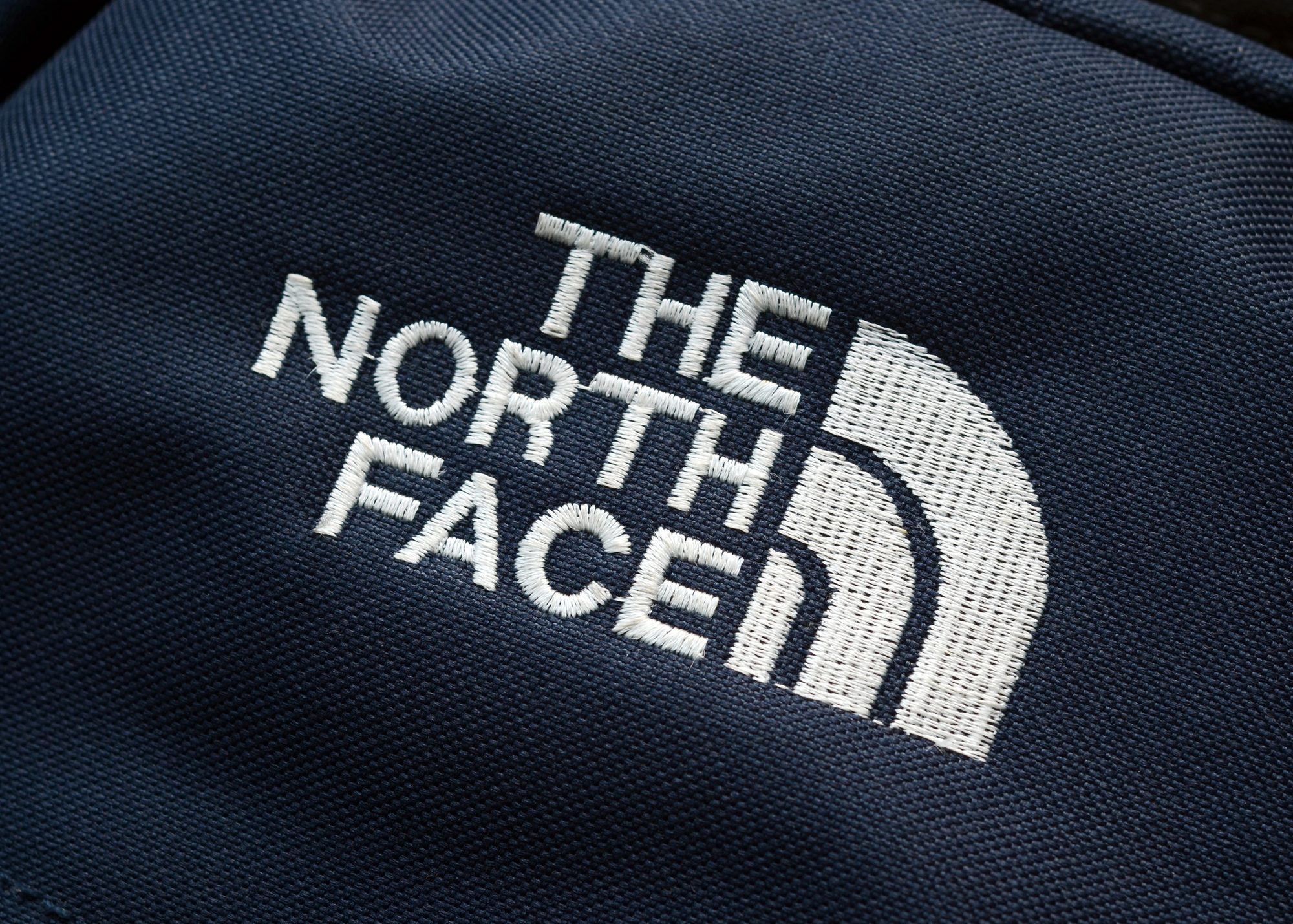 Close-up of The North Face logo embroidered in white on navy fabric.