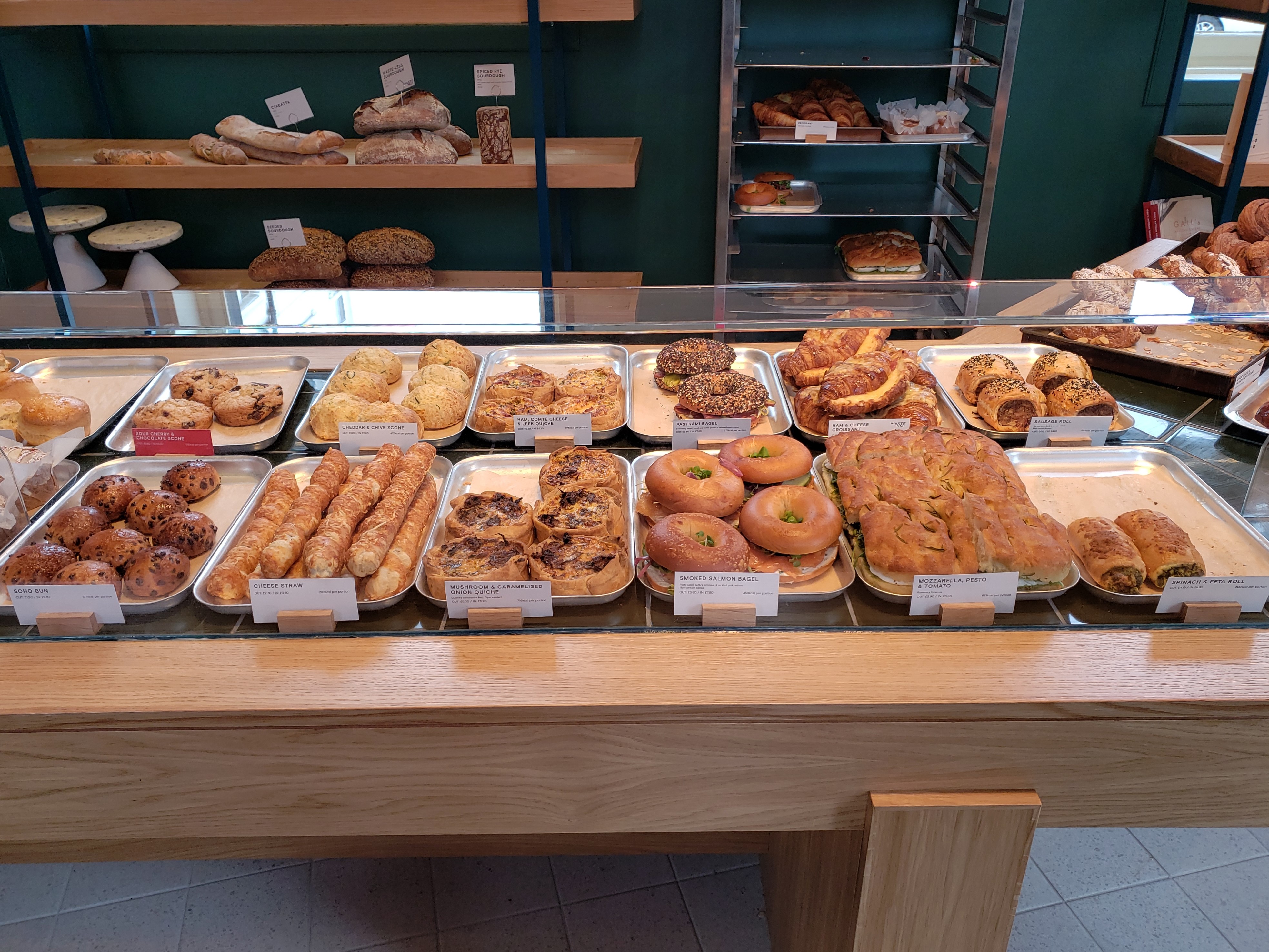 Bakery display counter with trays of pastries, croissants, and bread loaves on shelves behind.