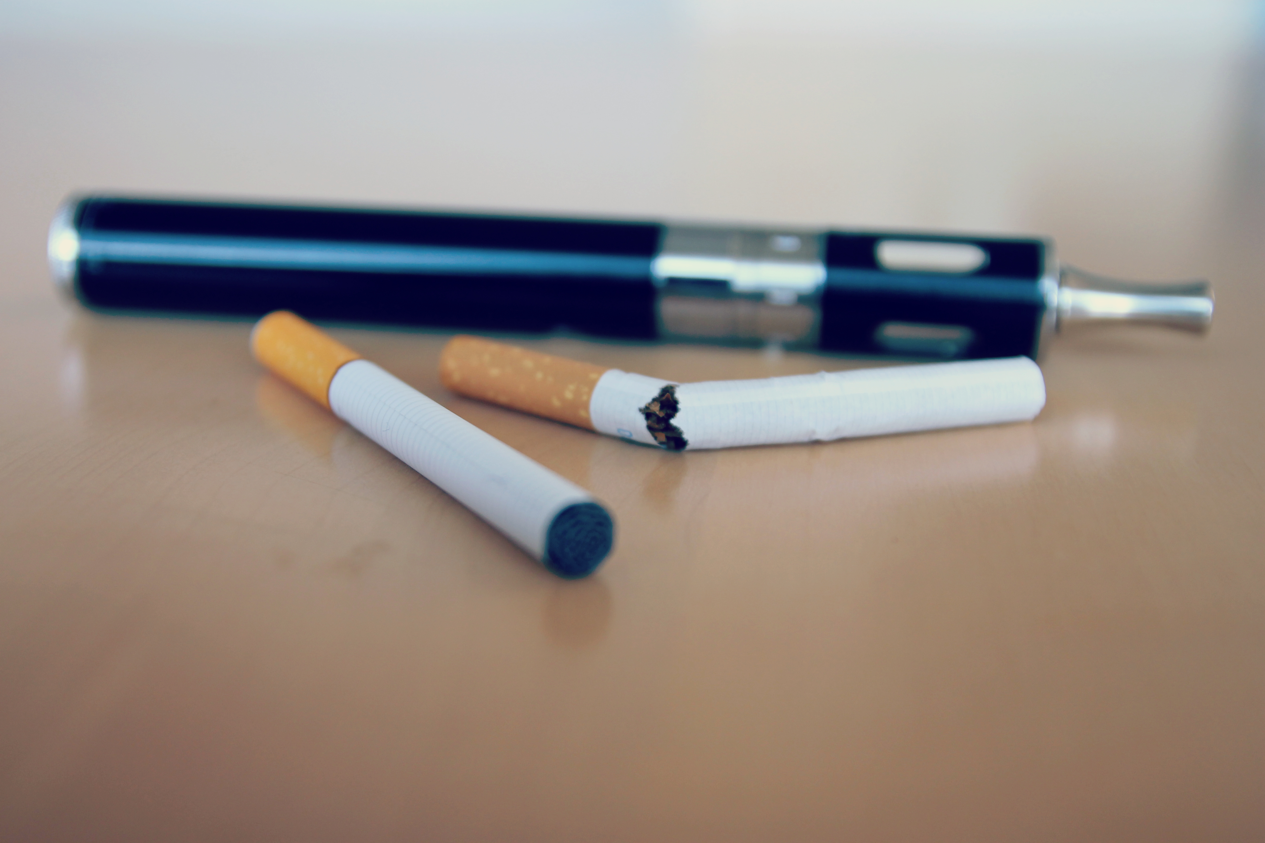 A black vape pen and two cigarettes resting on a wooden surface.