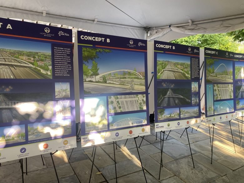 Display boards on easels under a tent showing architectural renderings of bridge design concepts from multiple angles.