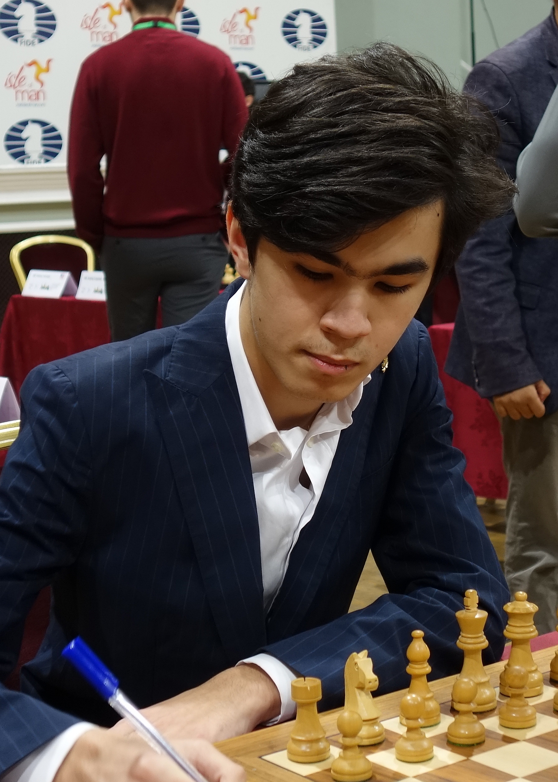 Young chess grandmaster in a navy pinstripe suit focused on a tournament chess board.