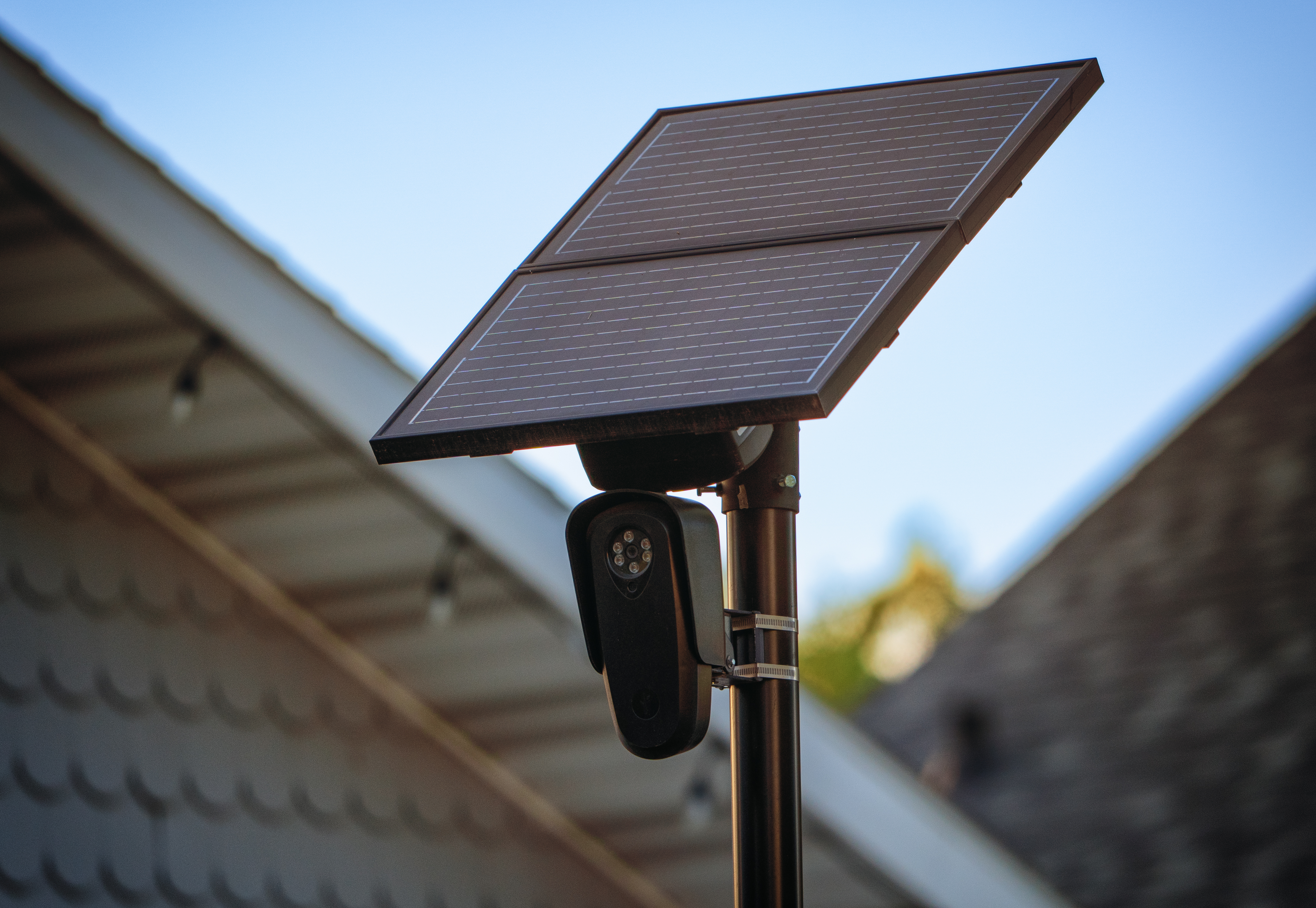 Solar-powered Flock Safety license plate reader camera on a pole with a residential roofline behind it.