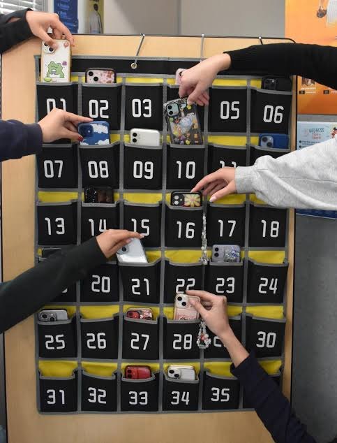 Hands inserting smartphones into a numbered fabric wall pocket organizer.