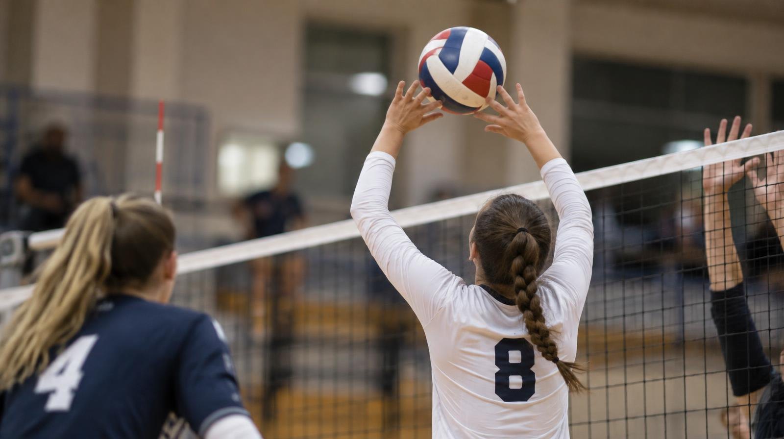 A volleyball in flight over the net on a hardwood gymnasium court.