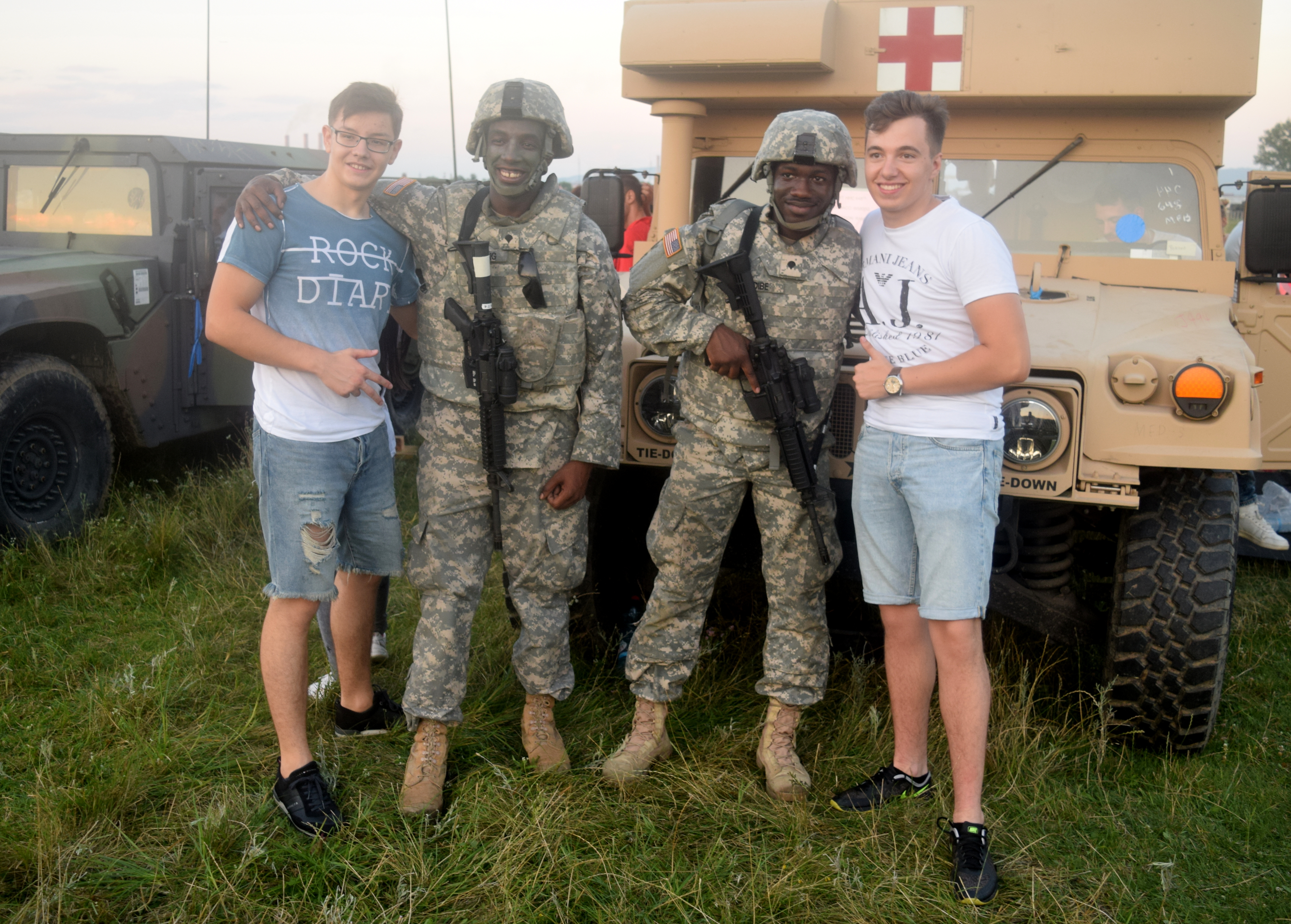 Two civilians and two uniformed soldiers smile together outdoors near a military Humvee at a community event.