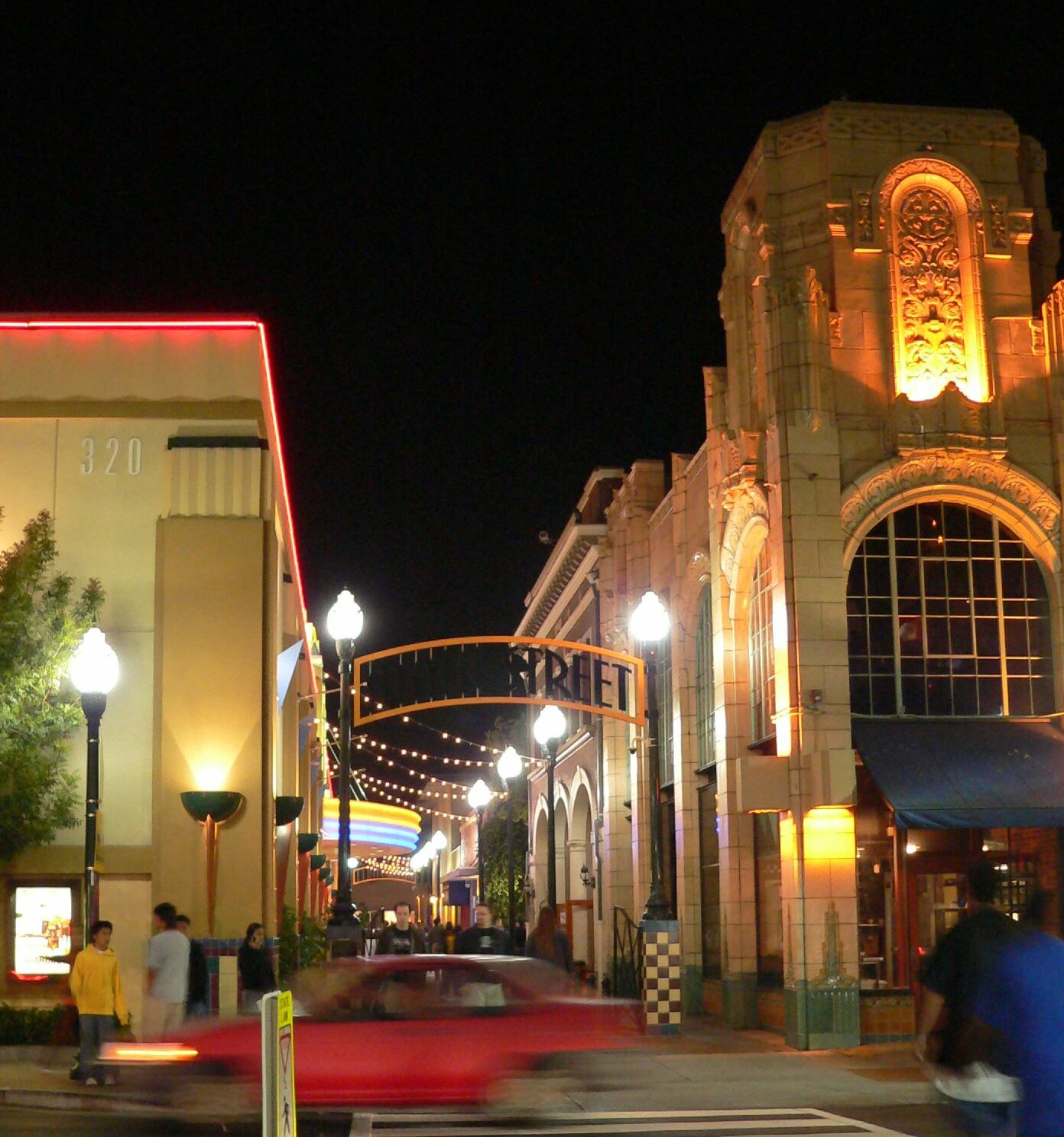Nighttime pedestrian corridor with string lights on an archway and glowing storefronts.
